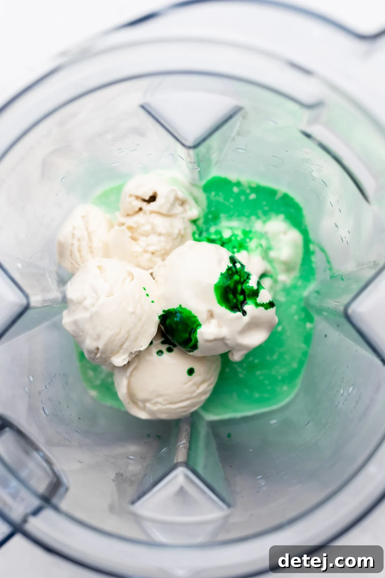 The vibrant green ingredients for a vegan shamrock shake are visible inside a clear blender jar, poised for blending.