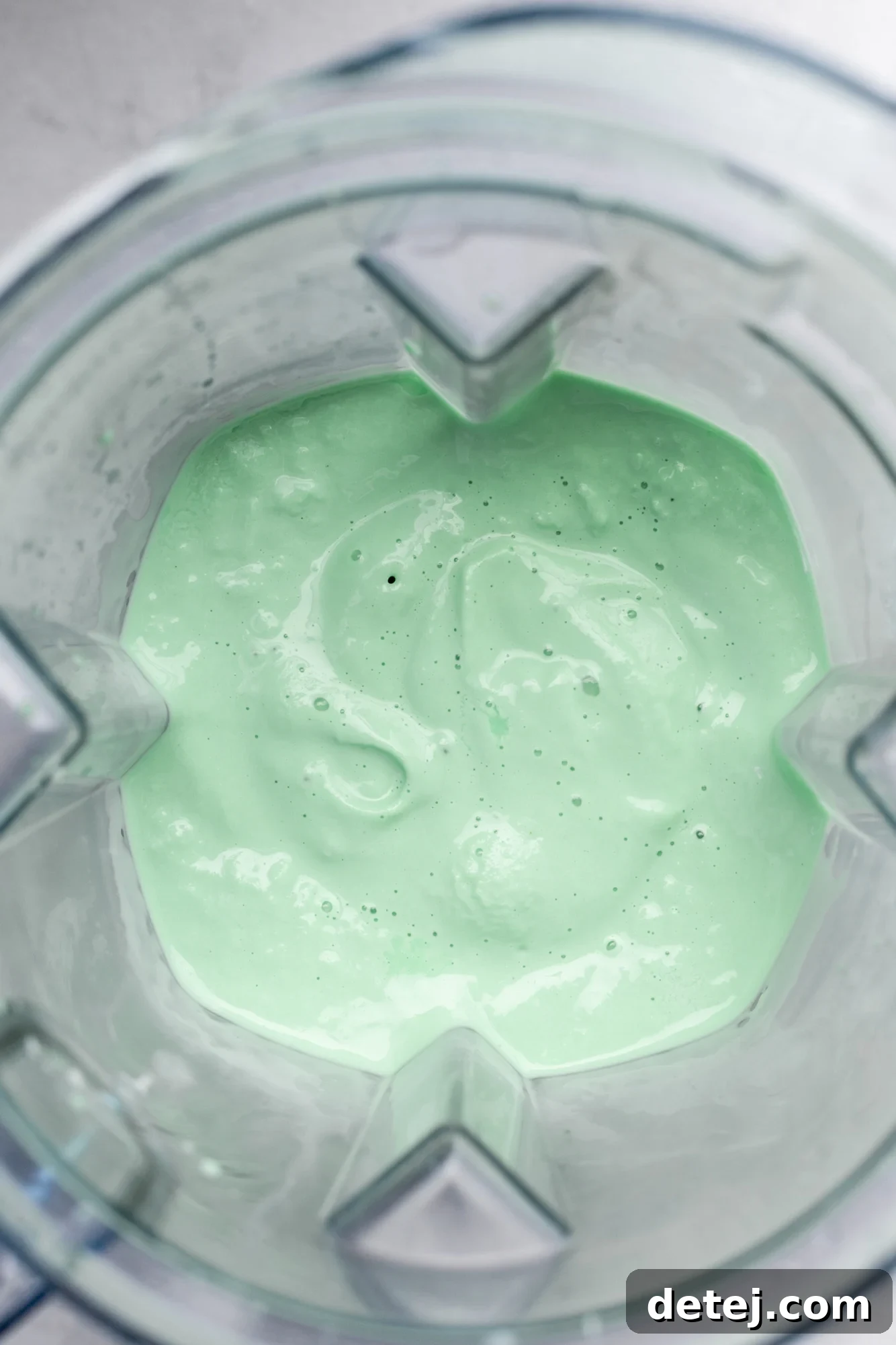 A perfectly blended, creamy mint green vegan shamrock shake swirls within a blender, ready to be poured and enjoyed.