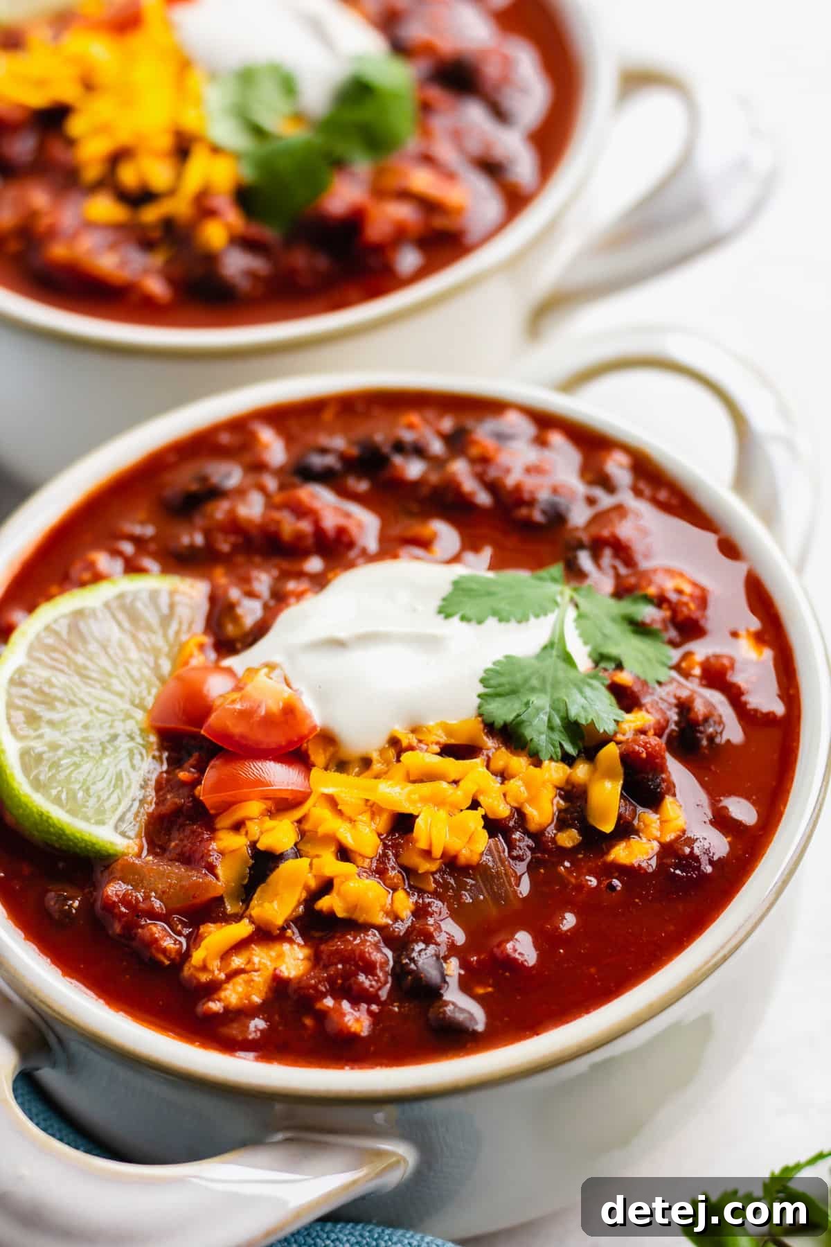 close up of a bowl with bean chili, sour cream, cheese and a lime wedge.