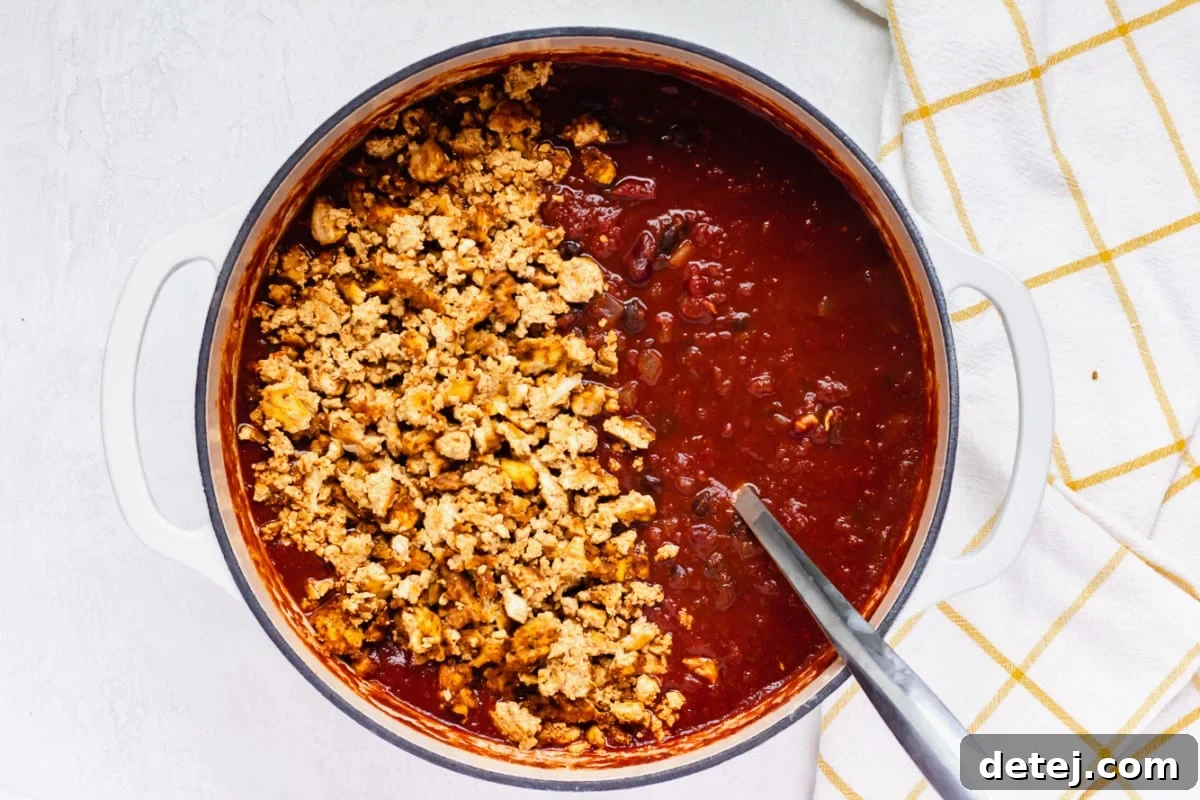 adding cooked crumbed tofu to the pot with the chili
