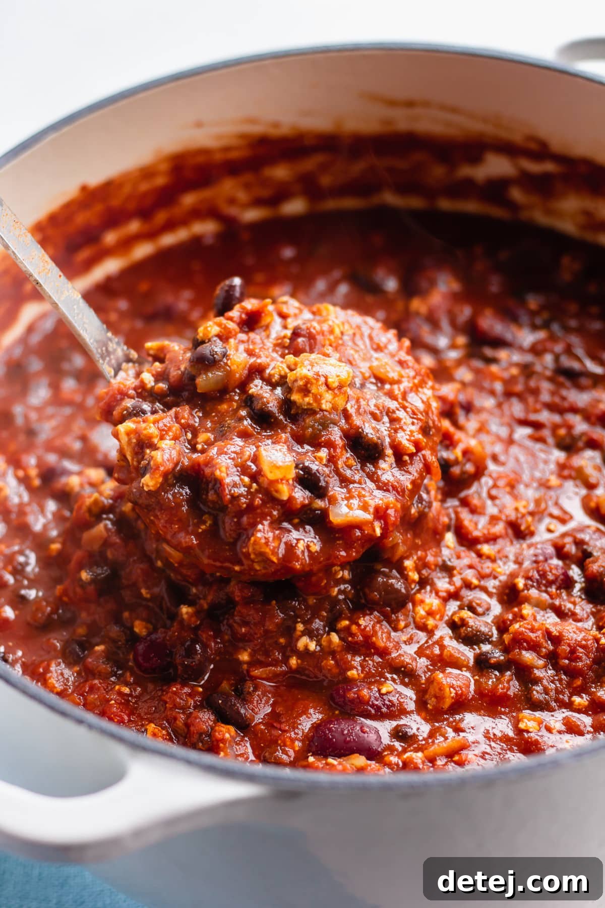 white pot full of vegan chili, a ladle scooping out a serving.