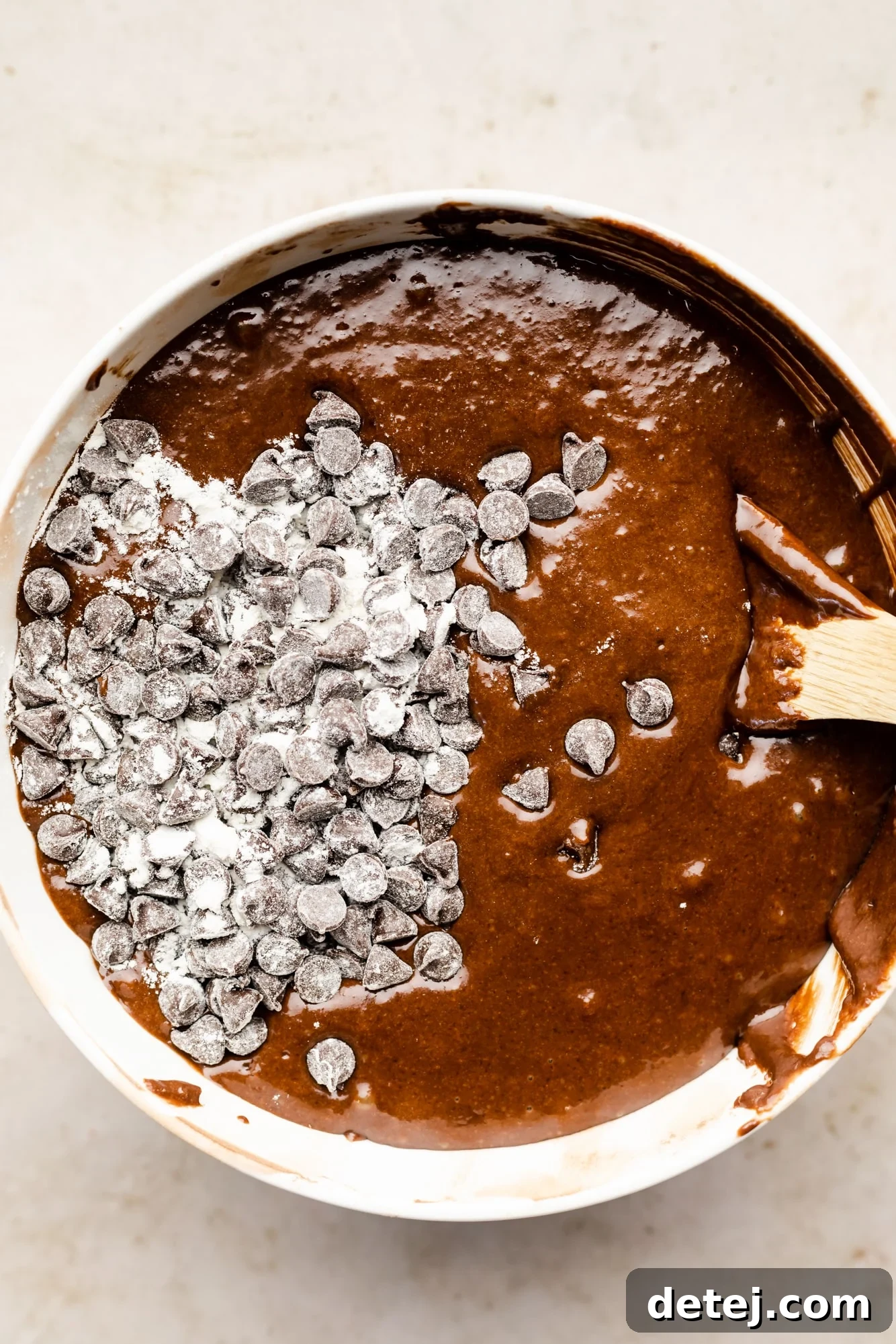 Decadent Chocolate Peanut Butter Dream 7 using a wooden spoon to fold chocolate chips into chocolate cake batter.