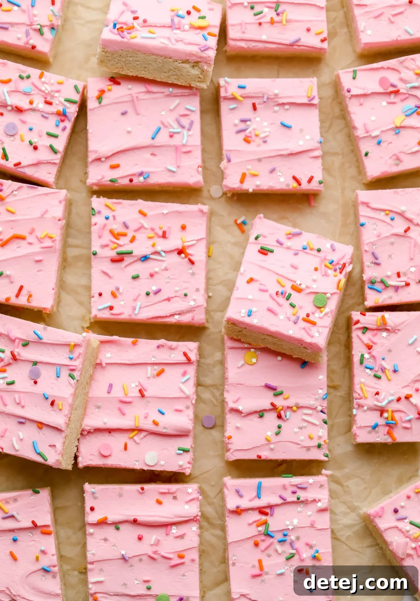 Rows of freshly baked vegan sugar cookie bars, generously adorned with vibrant pink frosting and a scattering of cheerful rainbow sprinkles.