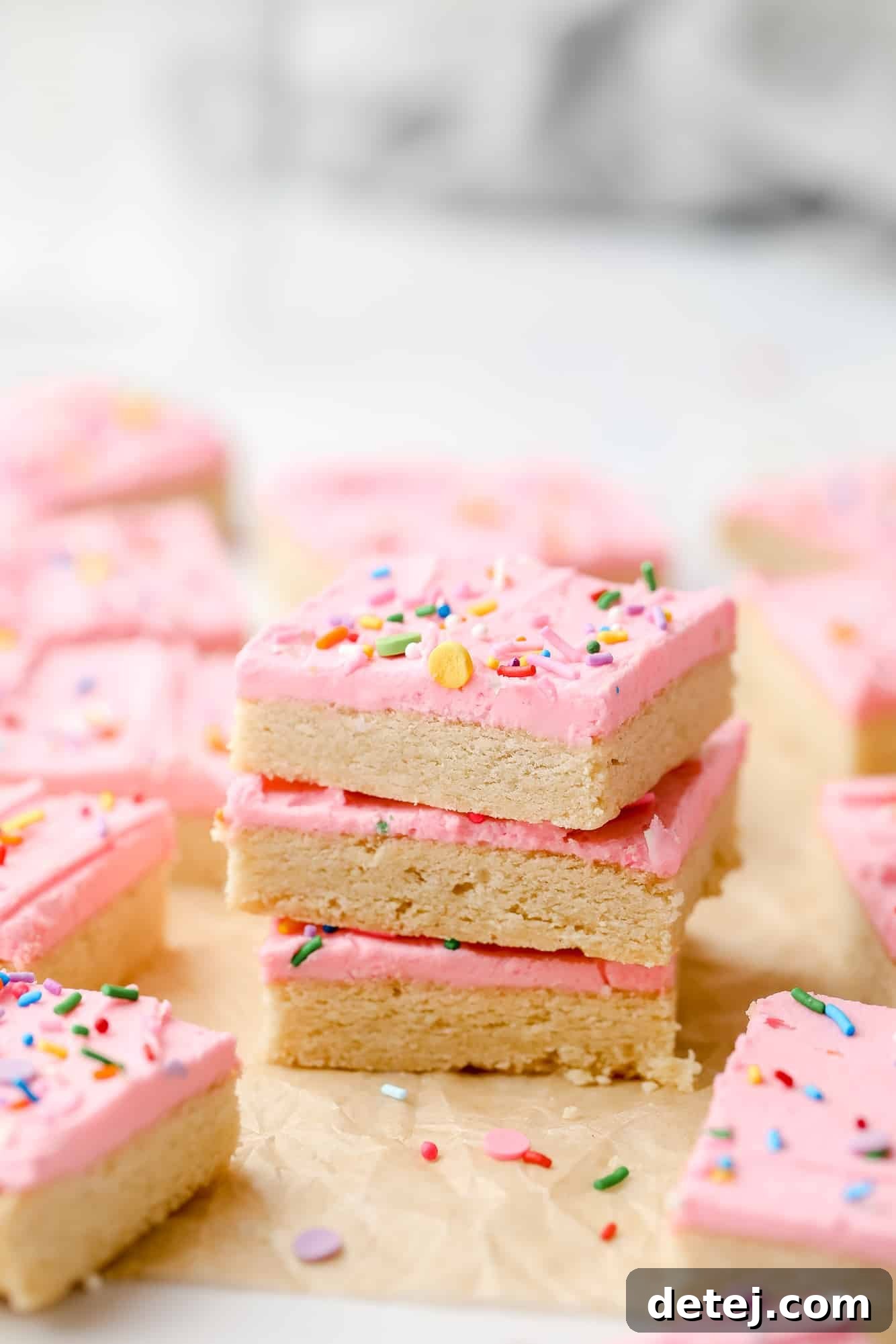 A stack of three vegan sugar cookie bars, each generously topped with fluffy pink frosting and colorful sprinkles, mirroring the first image but with a different angle.