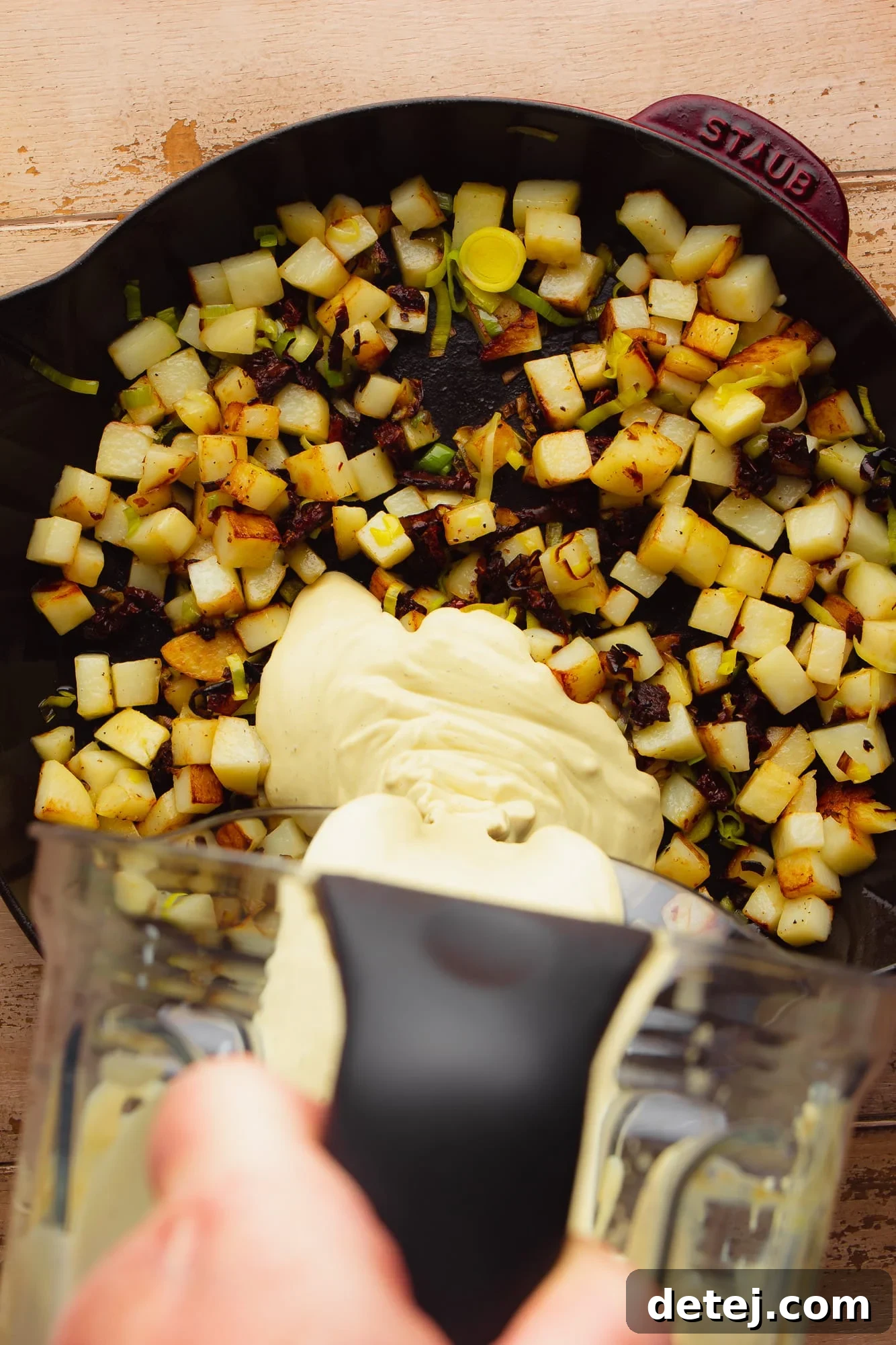 pouring a creamy yellow sauce over fried potatoes in a large black skillet.
