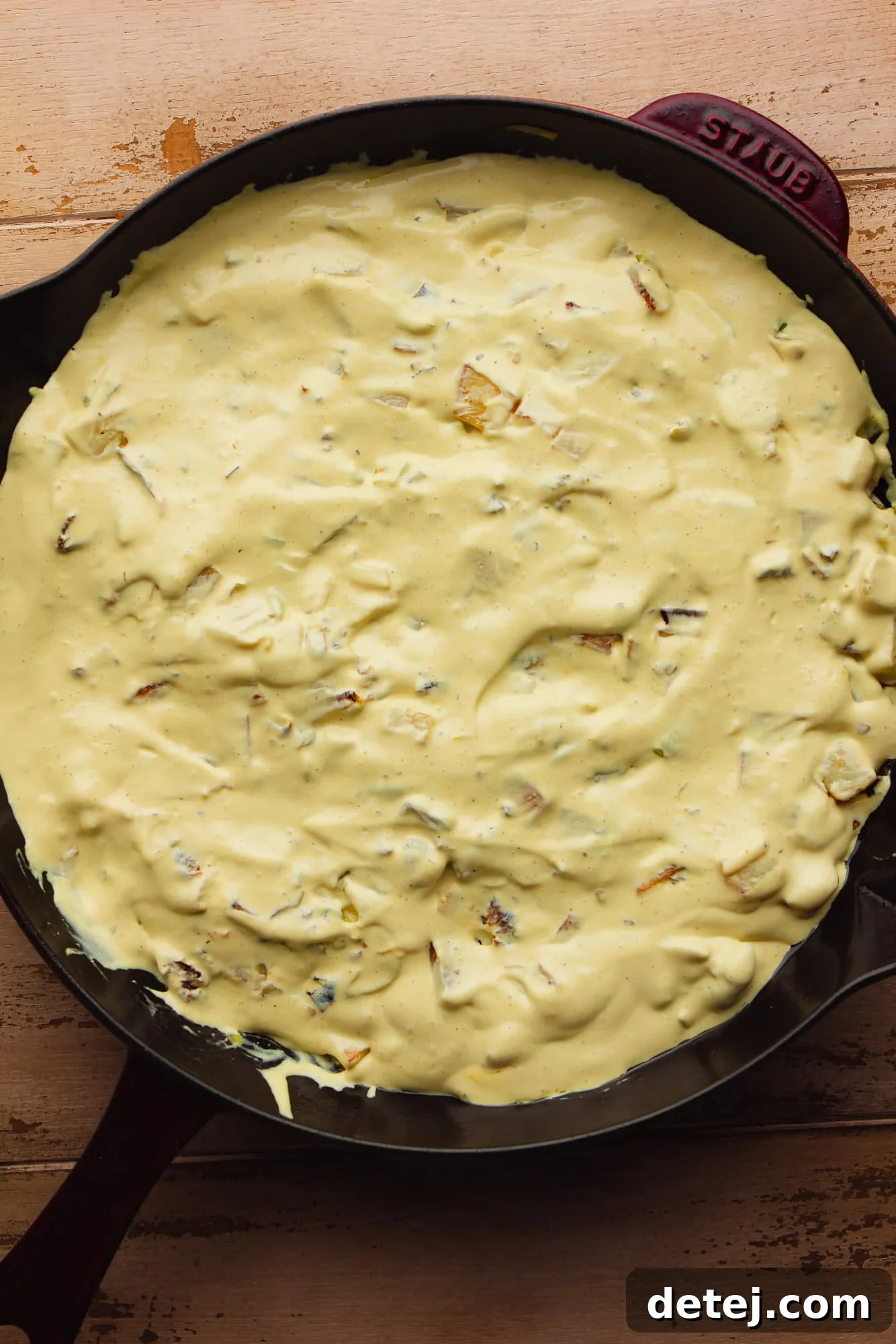 cooked vegetables topped with a creamy yellow sauce in a large black skillet.