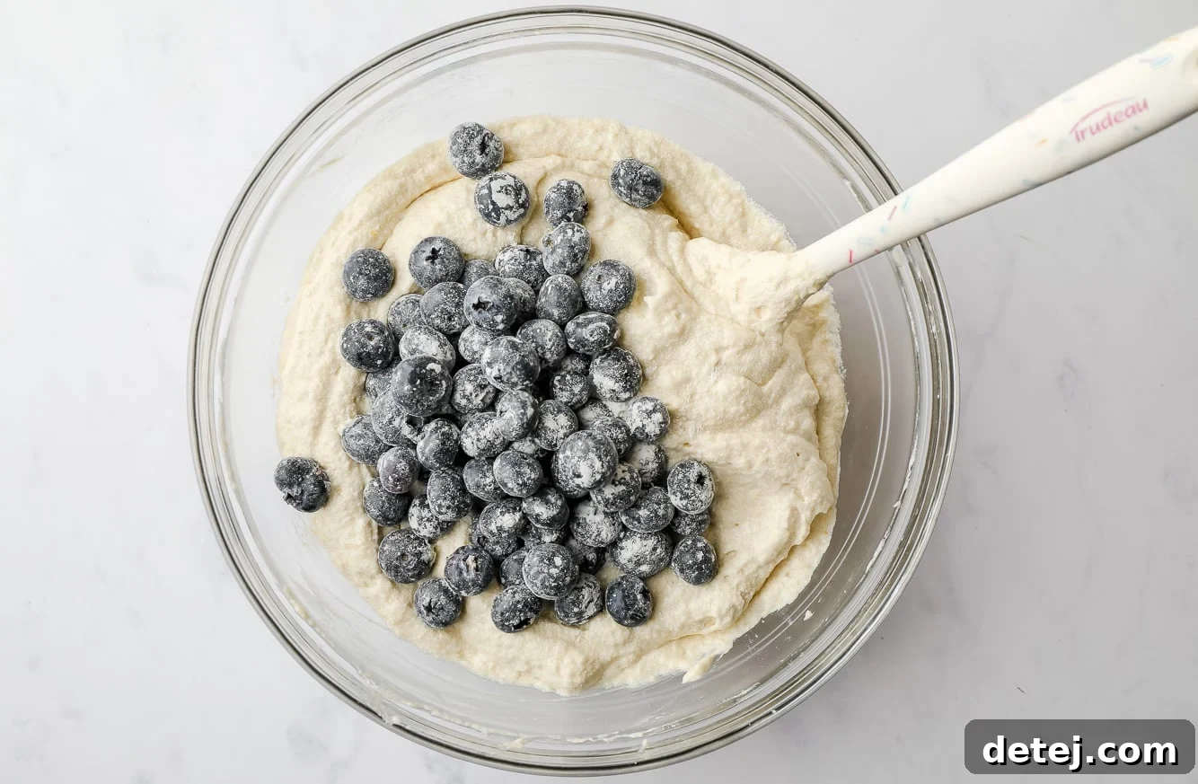 using a white spatula to fold blueberries into white cake batter.