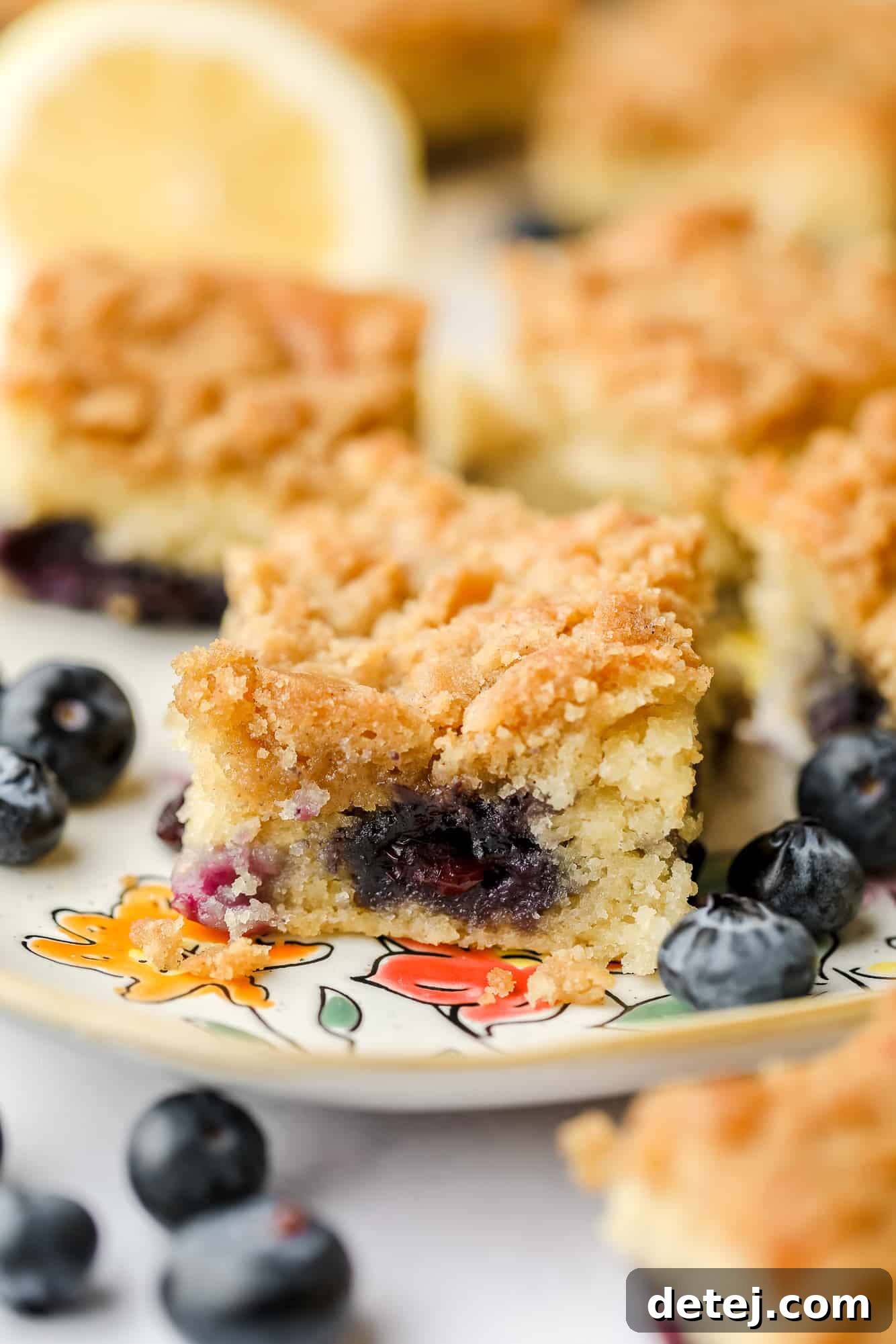 close up on a slice of blueberry coffee cake on a plate surrounded by fresh blueberries.