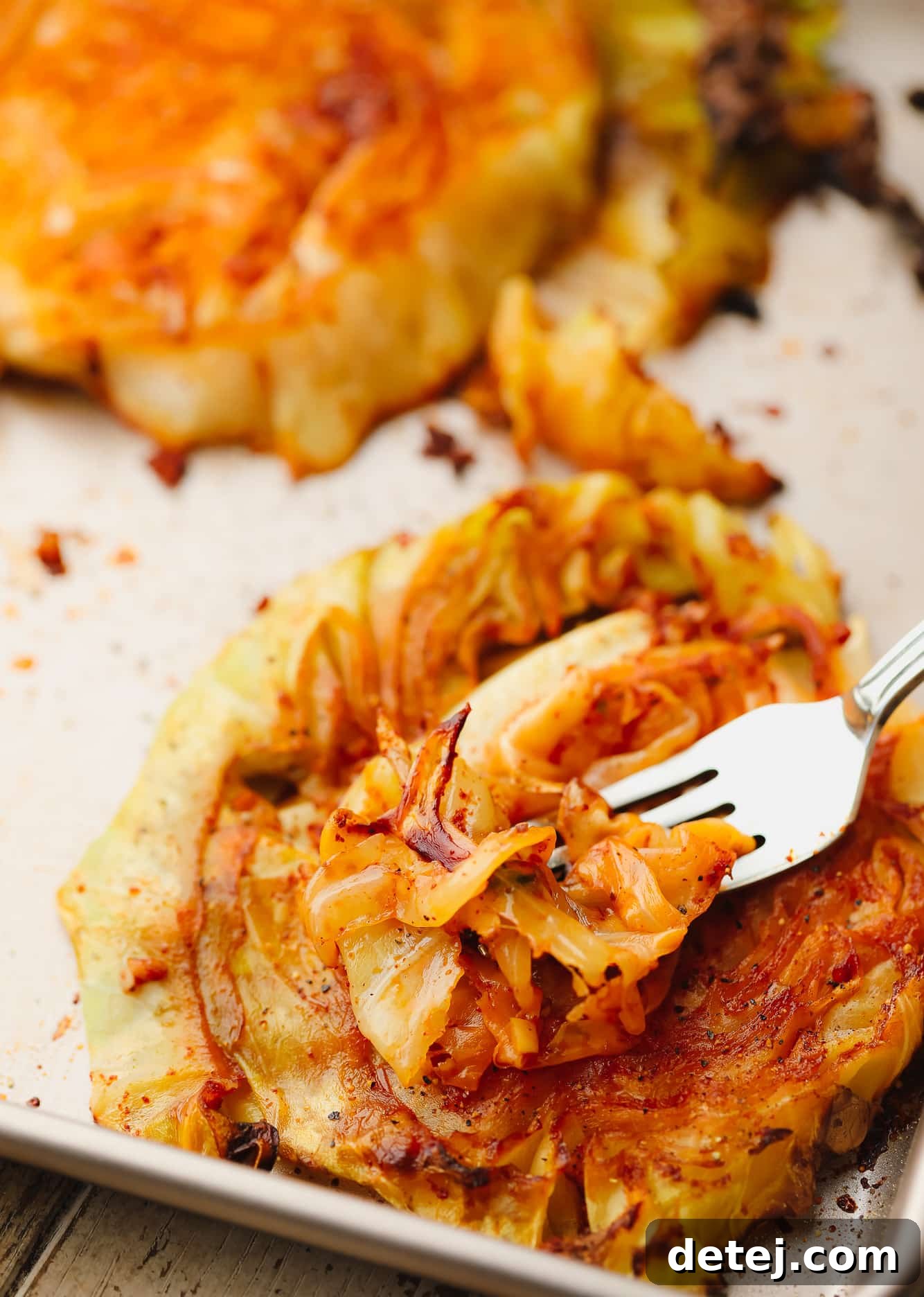 A metal fork scooping up a perfectly roasted and caramelized piece of cabbage from a cabbage steak, showcasing its tender texture.