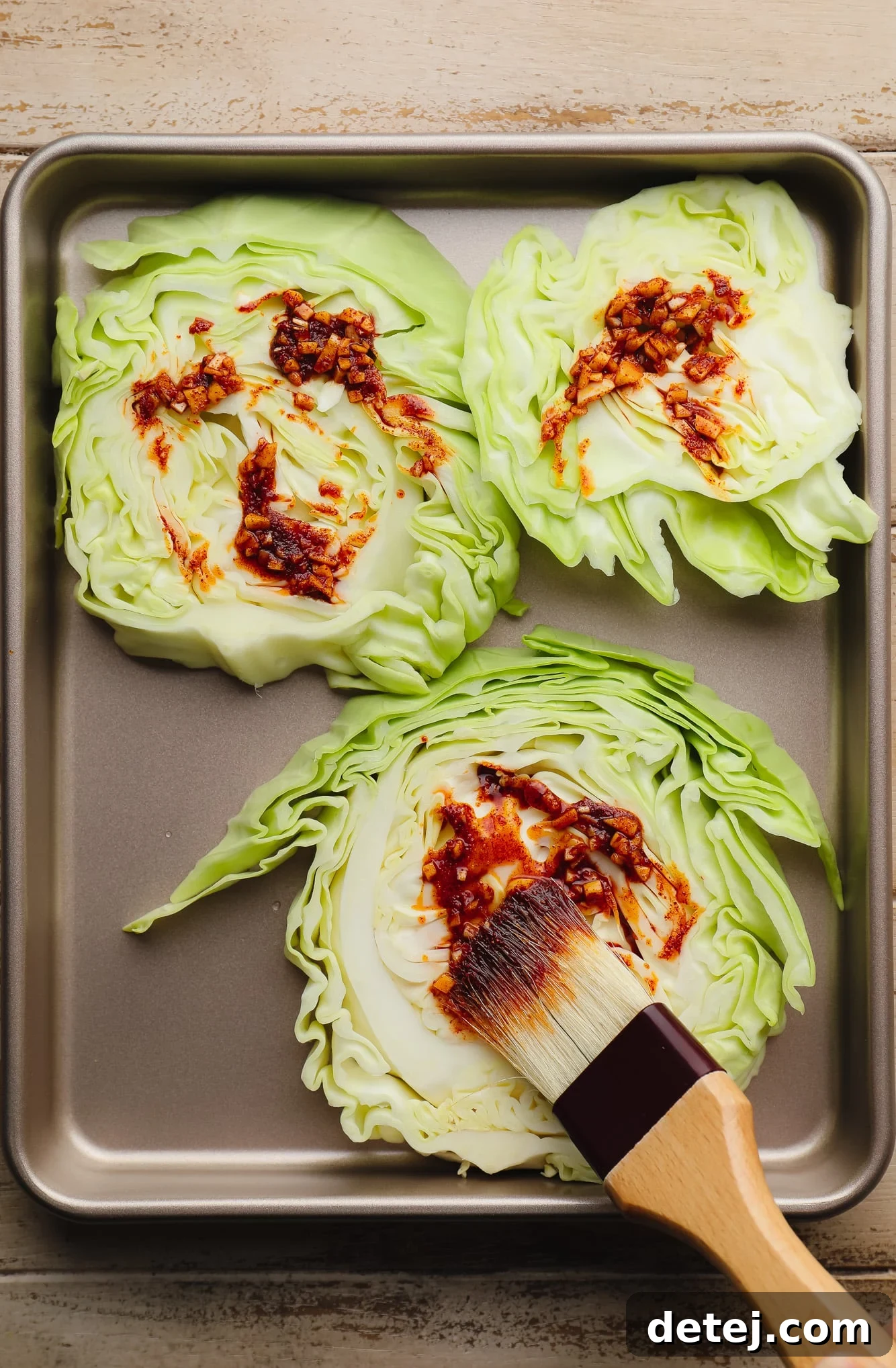 A close-up shot of a pastry brush applying a golden seasoning mixture onto a thick slice of raw cabbage, illustrating the coating process.
