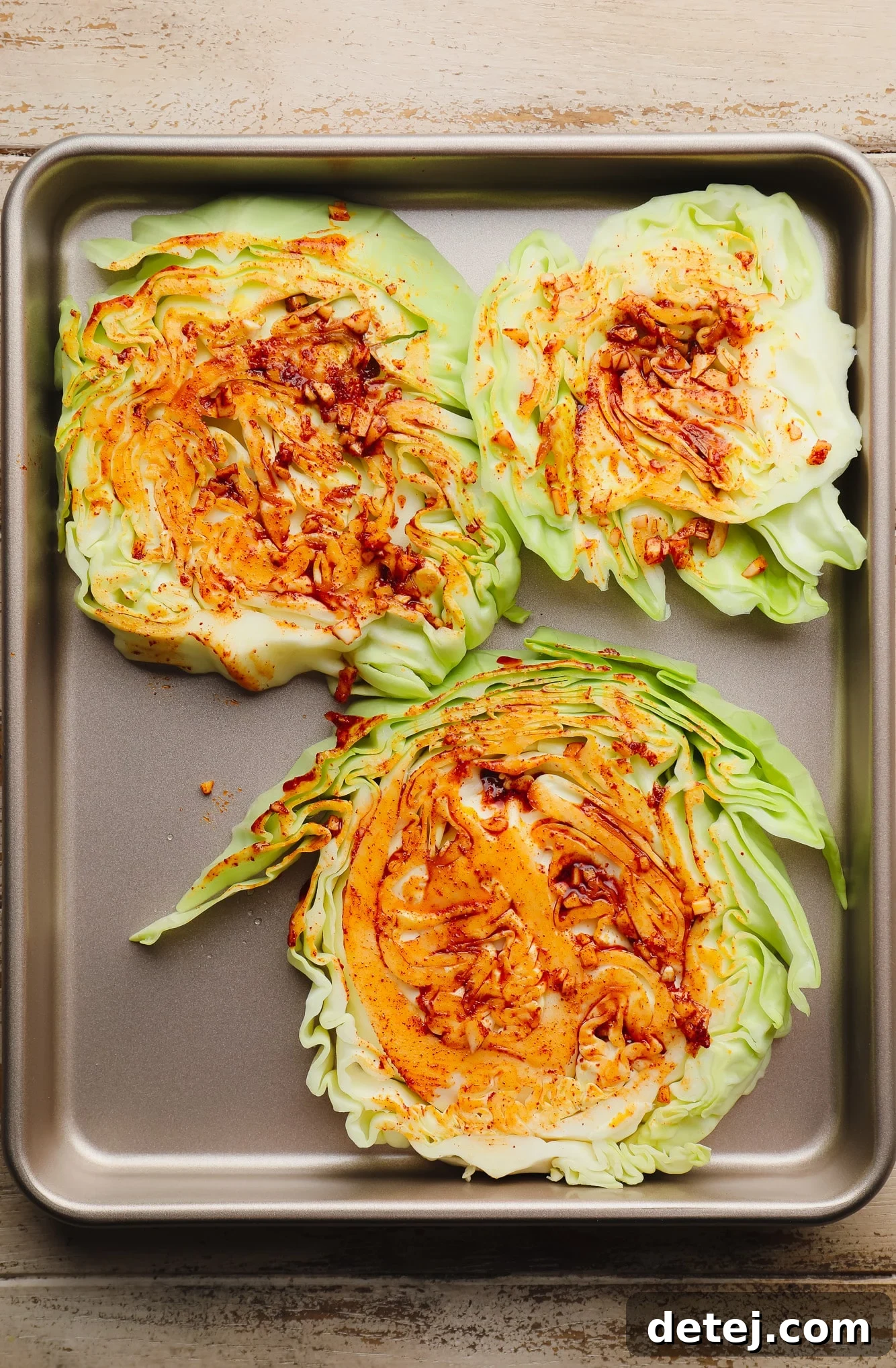 Several seasoned cabbage steaks laid out neatly on a metal baking sheet, glistening with oil and spices, ready to be roasted.