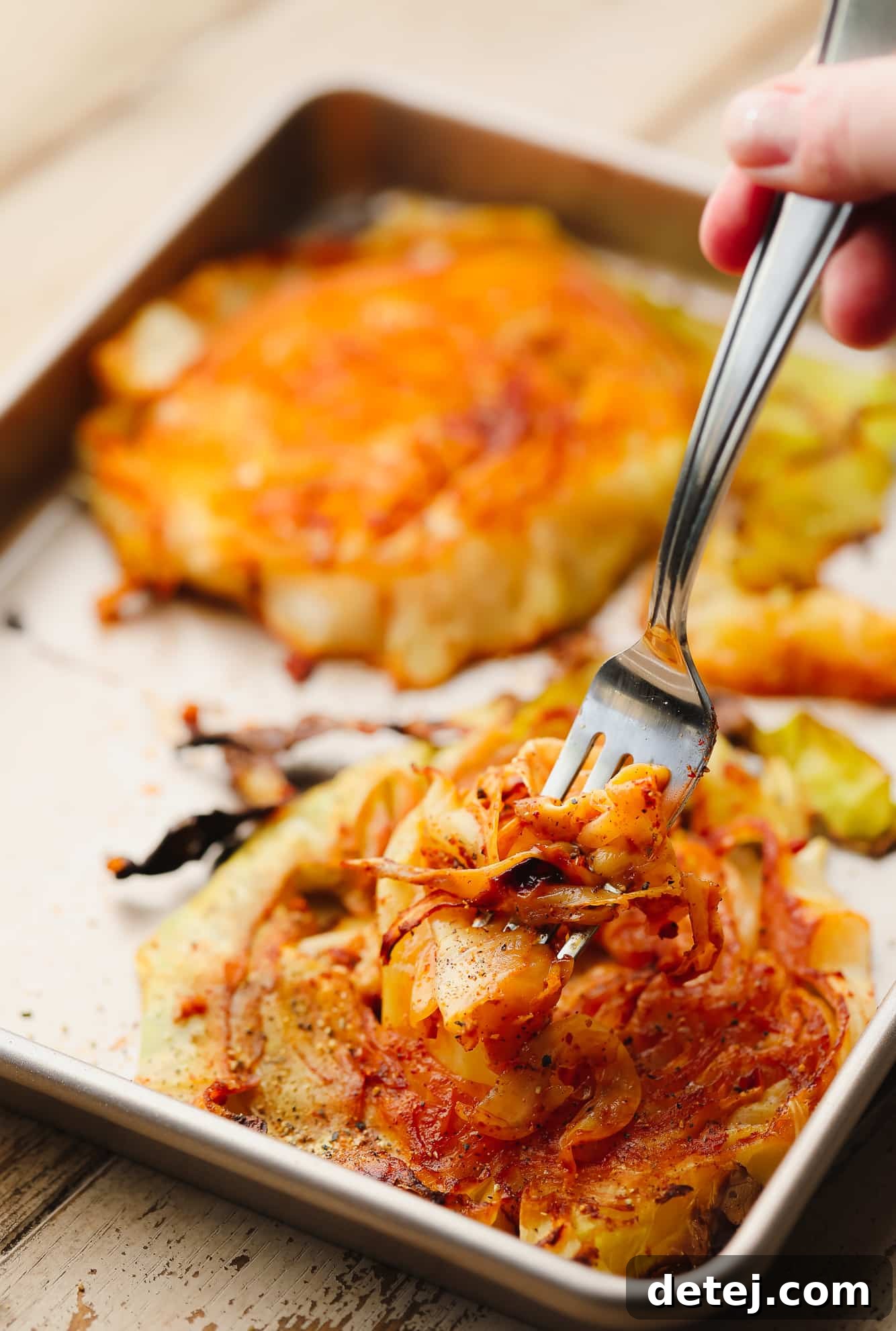 A metal fork delicately lifts a tender, golden-brown piece of roasted cabbage from a sliced cabbage steak, highlighting its appealing texture.