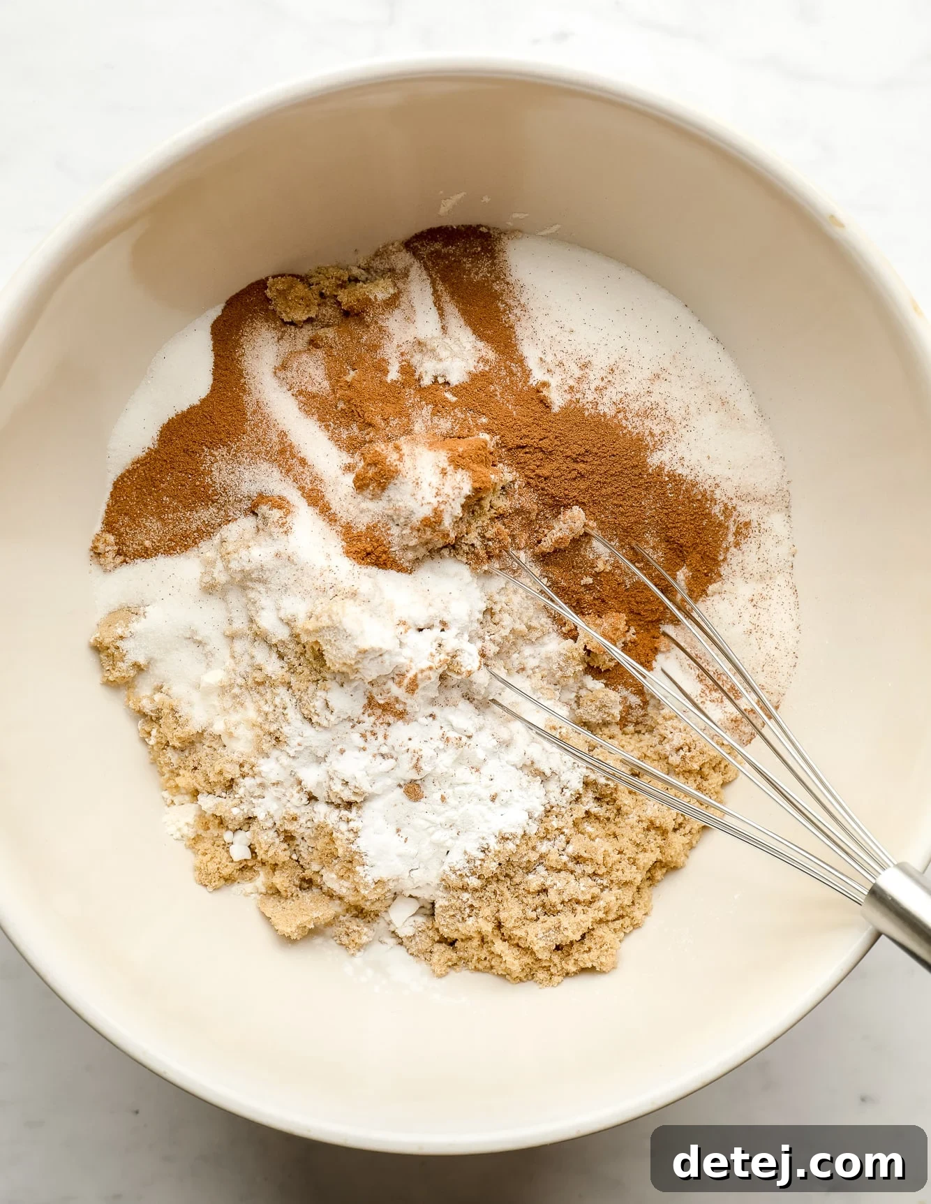 whisking flour, sugar, and spices together in a large white bowl for vegan hummingbird cake.