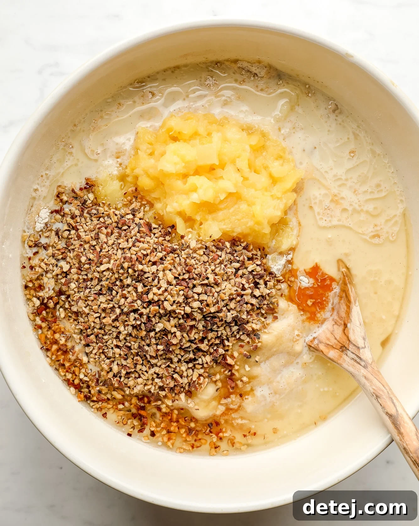 using a wooden spoon to stir hummingbird cake ingredients together in a large white bowl, showing the texture.