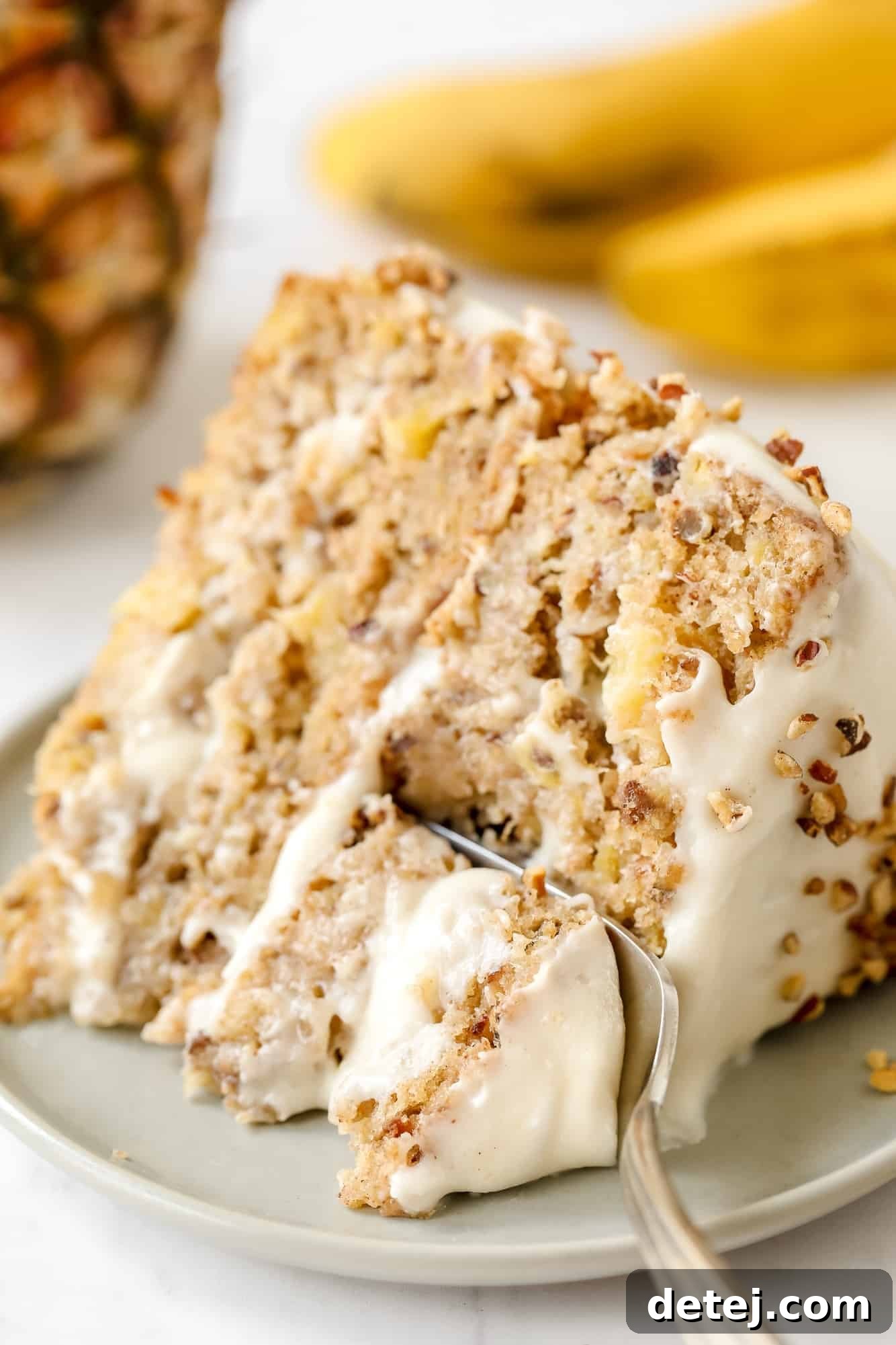 using a fork to take a bite from a slice of vegan hummingbird cake, showing the fluffy interior.