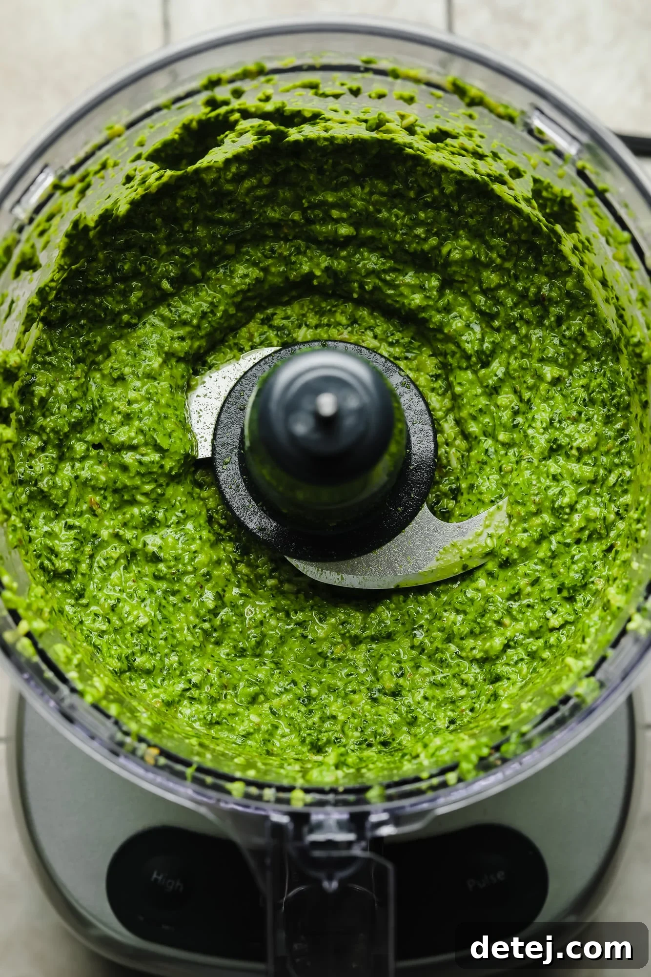 A close-up shot of a perfectly blended batch of vibrant green spinach pesto in a food processor, showcasing its smooth and creamy texture, ready to be scooped out.