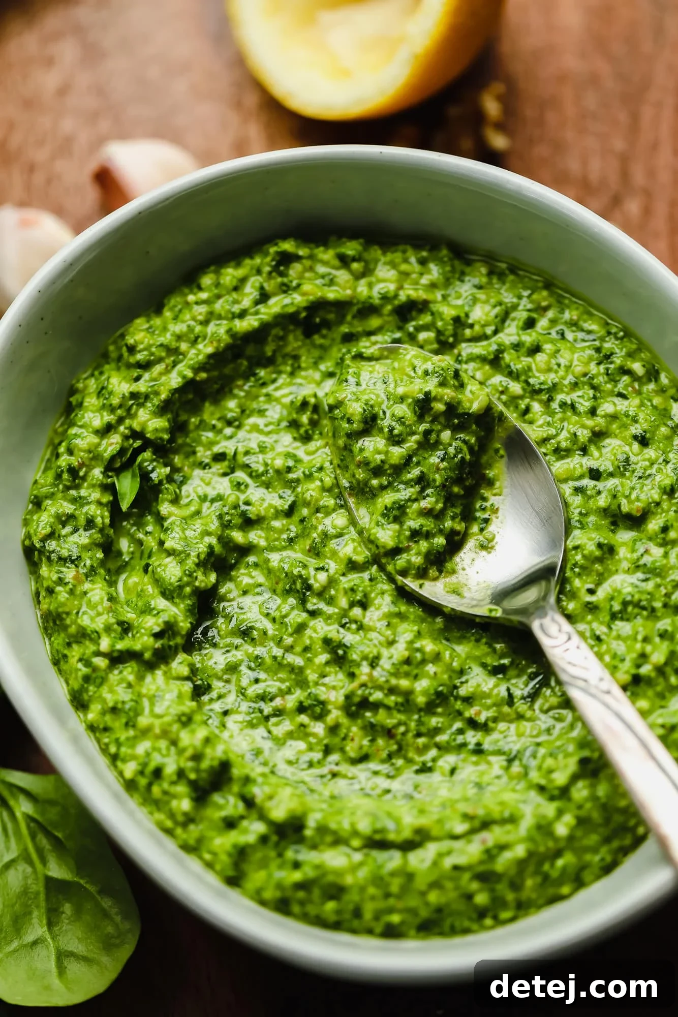 A beautifully presented grey bowl filled with vibrant green spinach pesto, with a sleek metal spoon resting delicately on top, ready to be served.