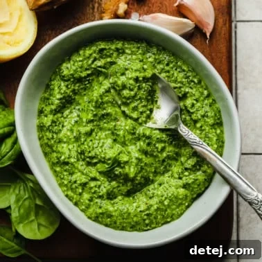 A grey bowl filled with spinach pesto with a metal spoon on top.