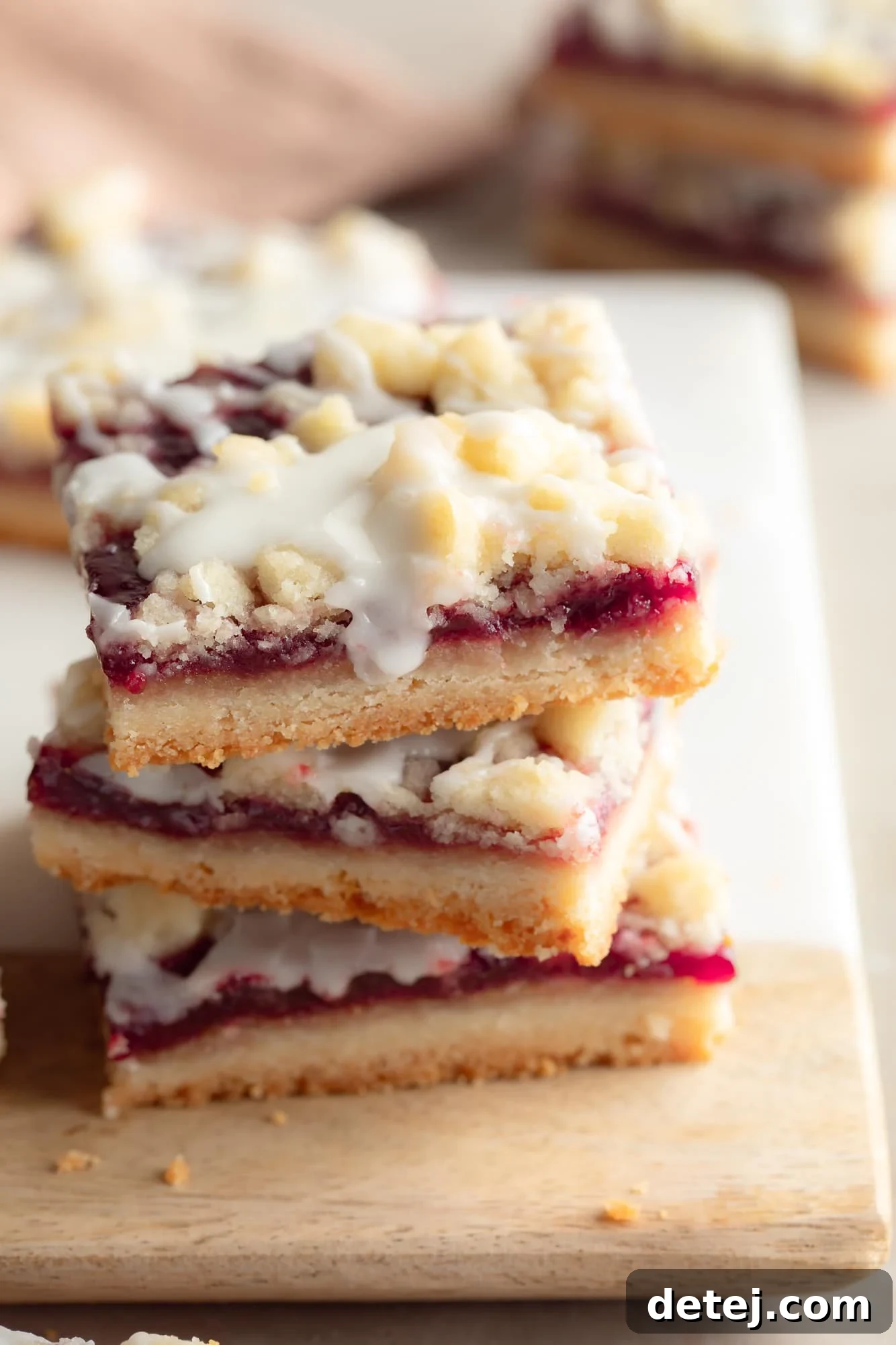 A close-up of a perfectly arranged stack of three vegan raspberry bars on a cutting board, highlighting the delicate layers of crumbly shortbread and sweet raspberry filling, ready to be enjoyed.