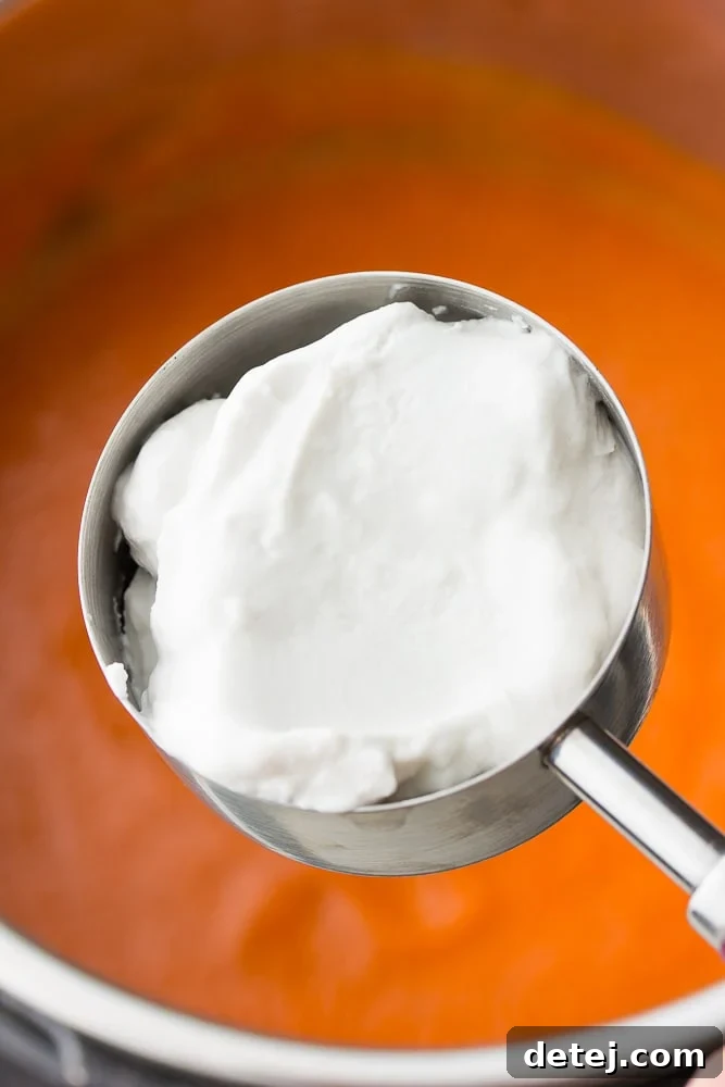 measuring cup with thick coconut cream being added to the blended Instant Pot tomato soup