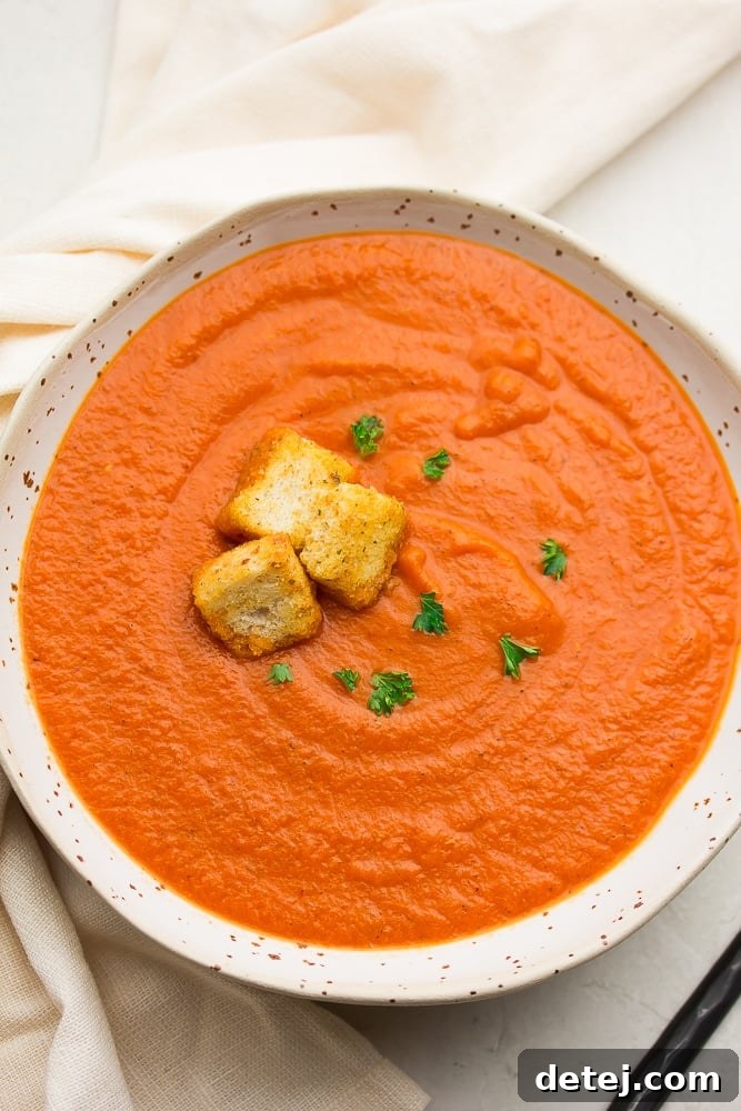 bowl of vibrant red-orange creamy vegan tomato soup topped with crunchy croutons