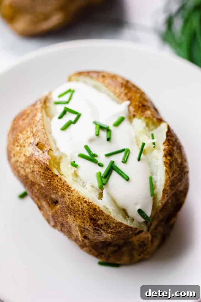 white plate with a baked potato, sour cream and chives