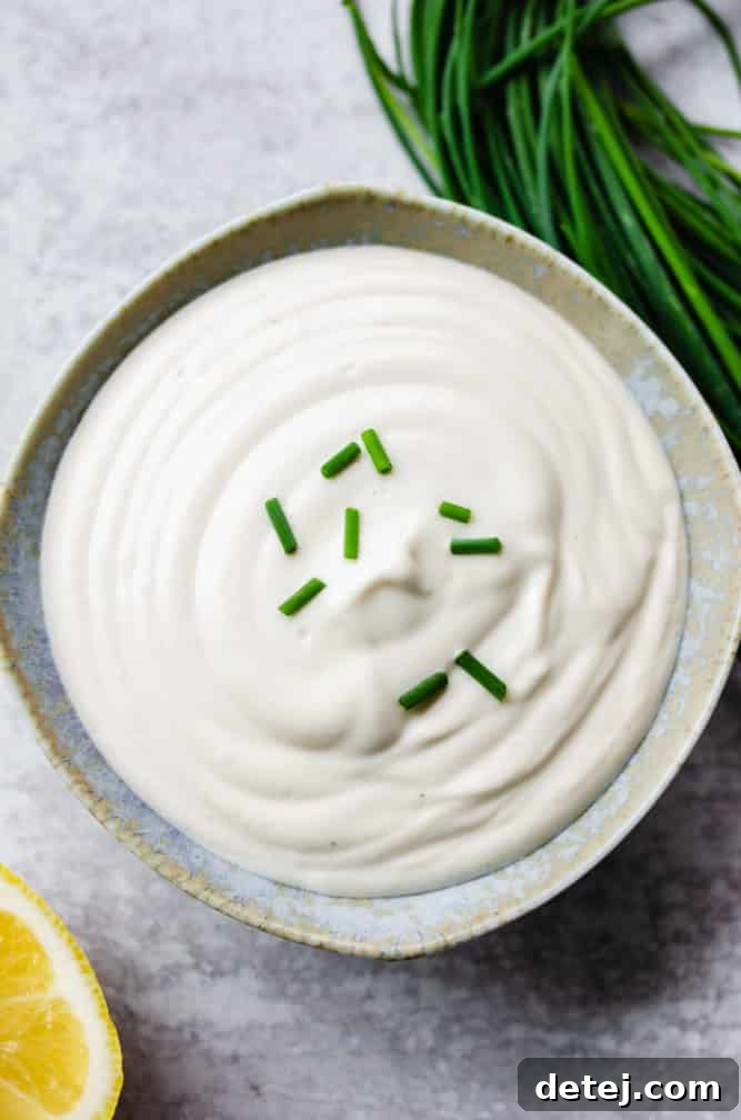 small speckled bowl of vegan sour cream with chives on top, grey background