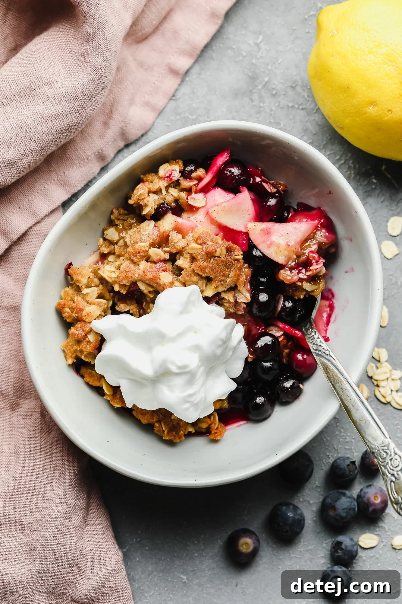 A glorious serving of vegan apple and blueberry crumble in a white bowl, topped with fluffy vegan whipped cream, ready to be enjoyed.