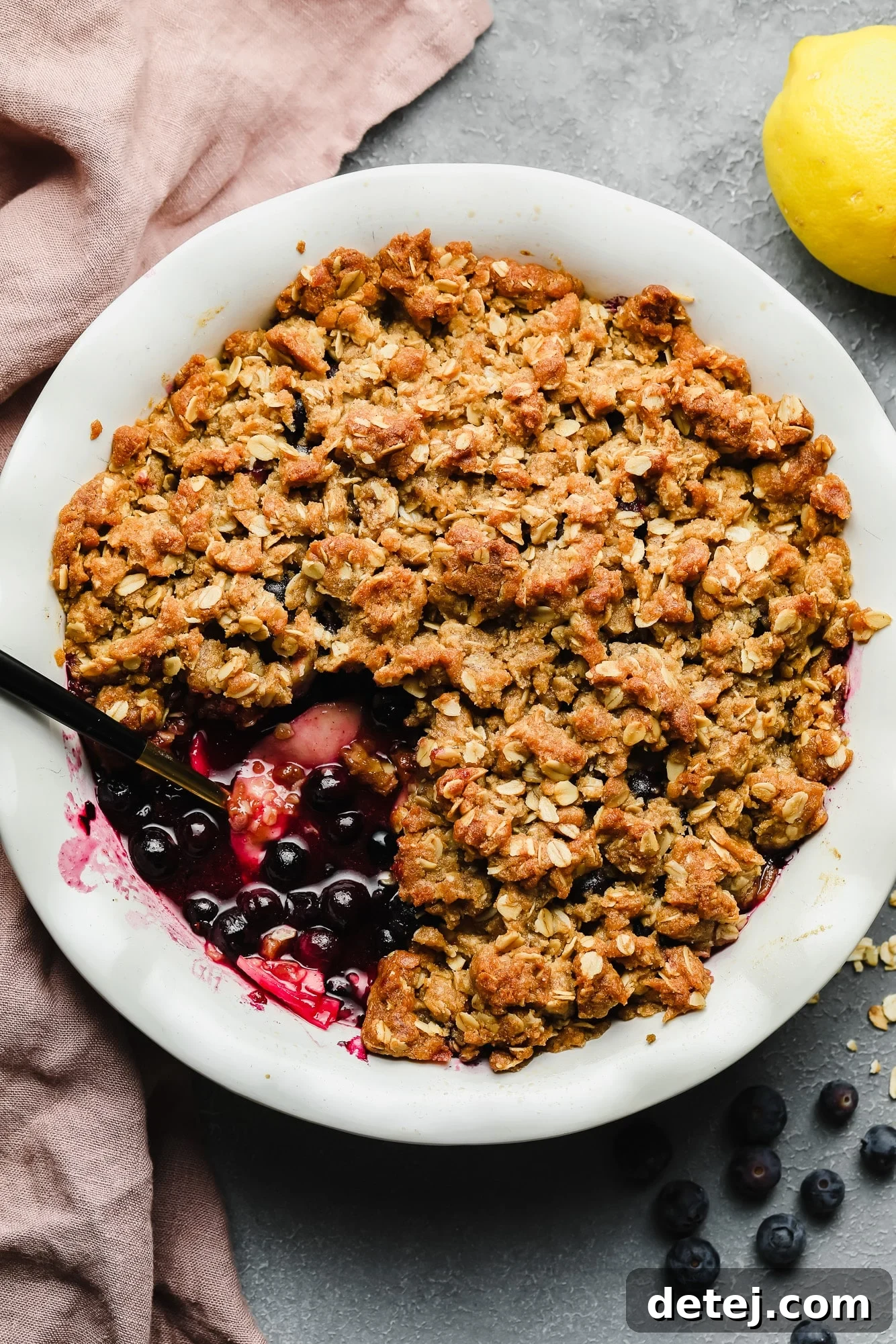 Close-up shot of a baked apple and blueberry crumble in a white bowl, showing its golden, crumbly topping and bubbling fruit filling.