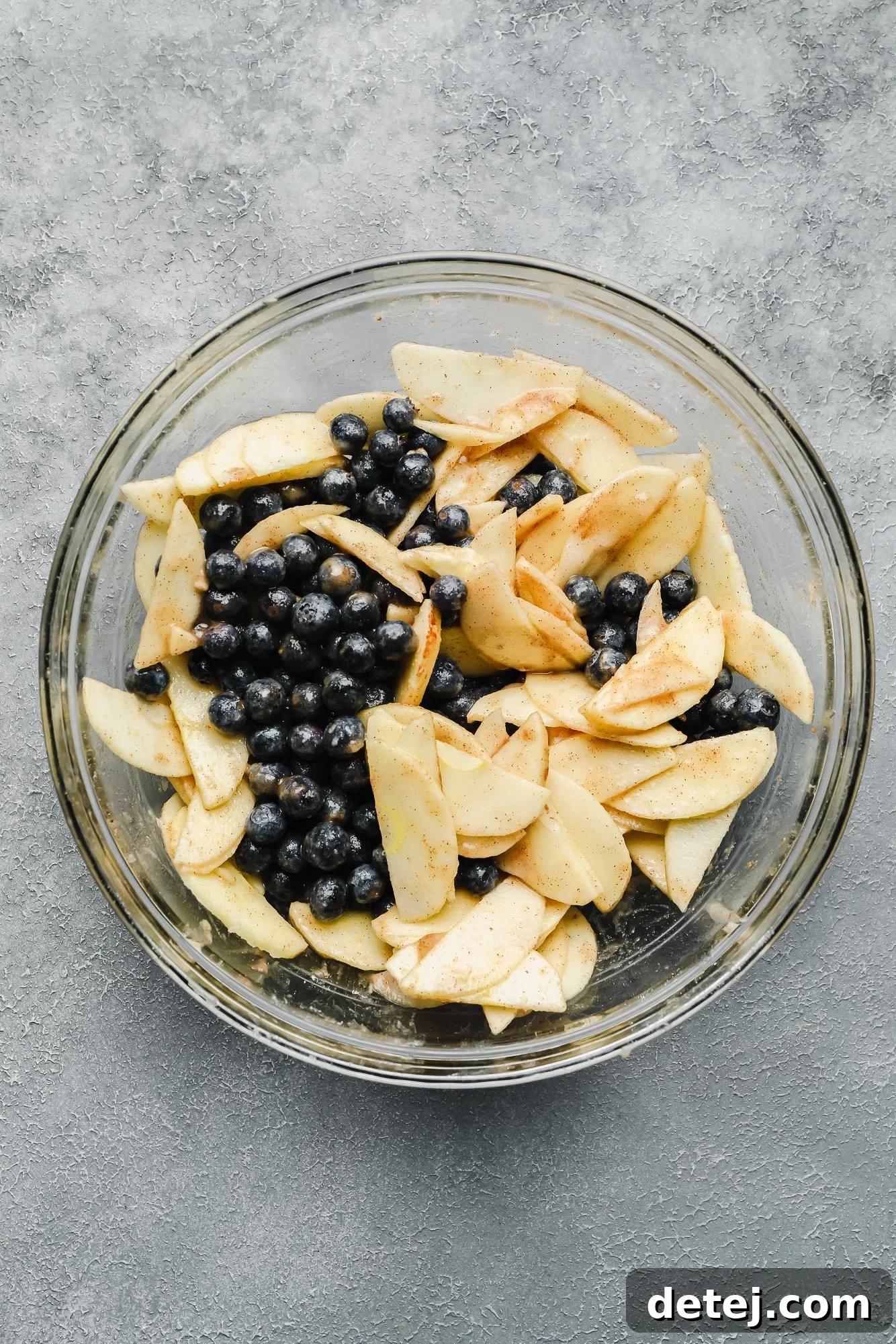 Fresh blueberries and thinly sliced apples in a glass bowl, ready to be combined for the crumble filling.