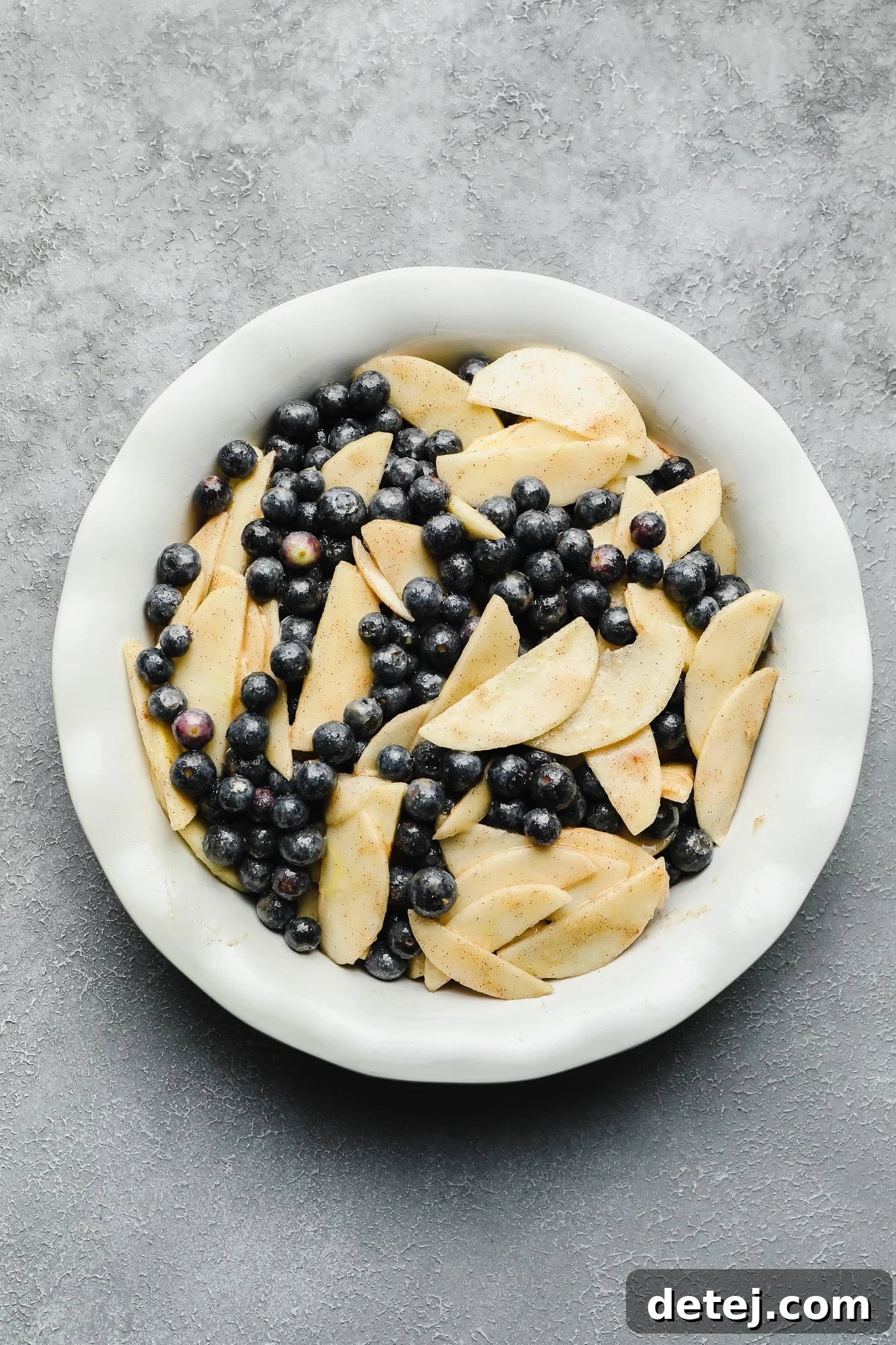 A bowl filled with fresh blueberries and thinly sliced apples, coated in sugar and spices, ready for the baking dish.