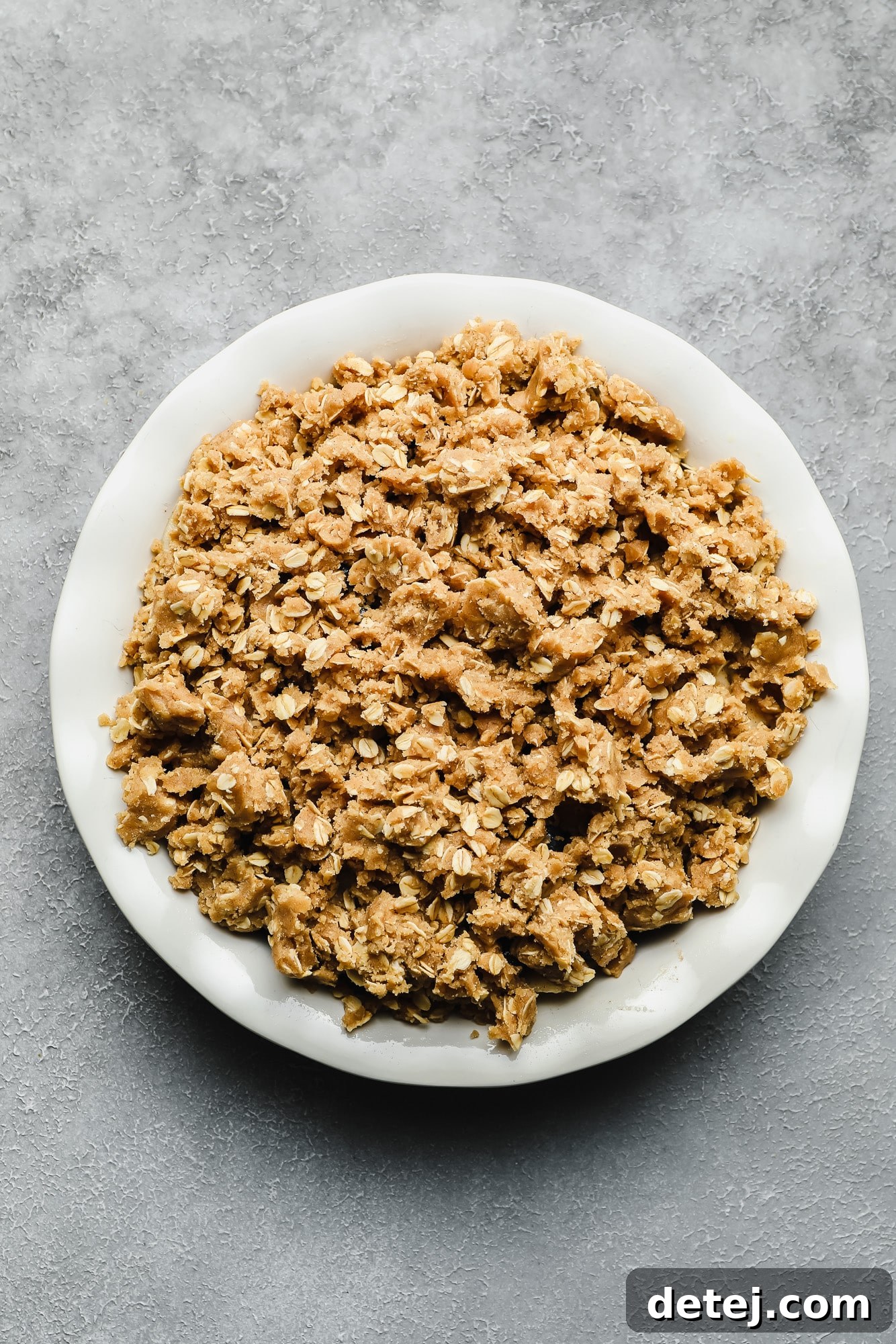 A close-up view of the golden, buttery, and oat-filled crumble topping in a white bowl, showcasing its perfect texture.