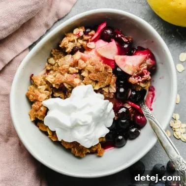 a serving of apple and blueberry crumble in a white bowl with vegan whipped cream on top.