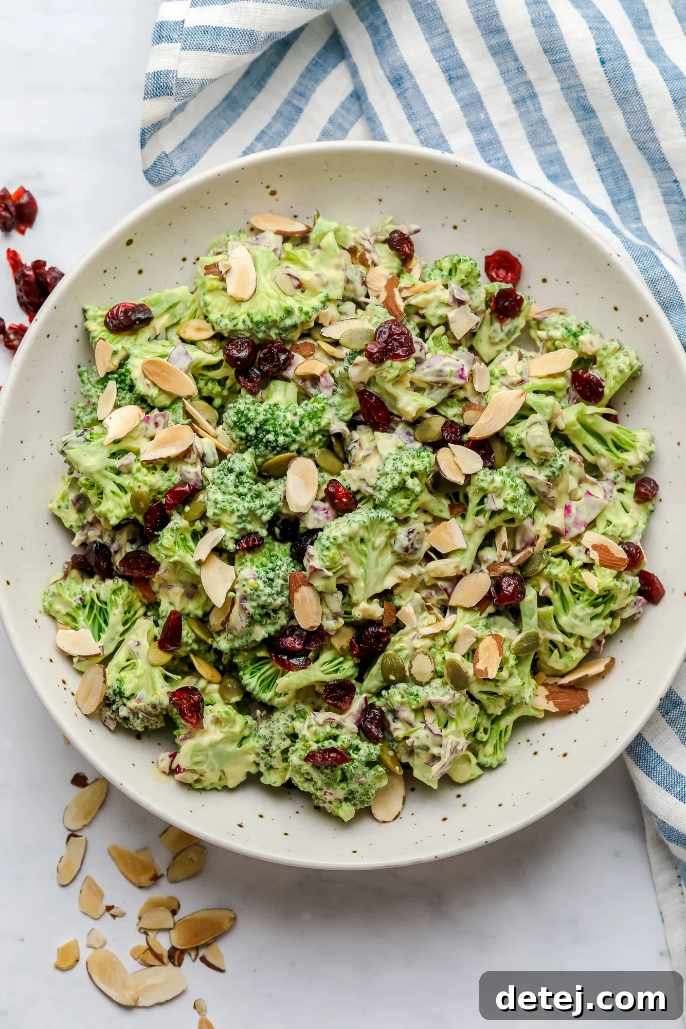 Vibrant vegan broccoli salad tossed in a creamy cashew dressing, garnished with sliced almonds, served in a large white bowl.