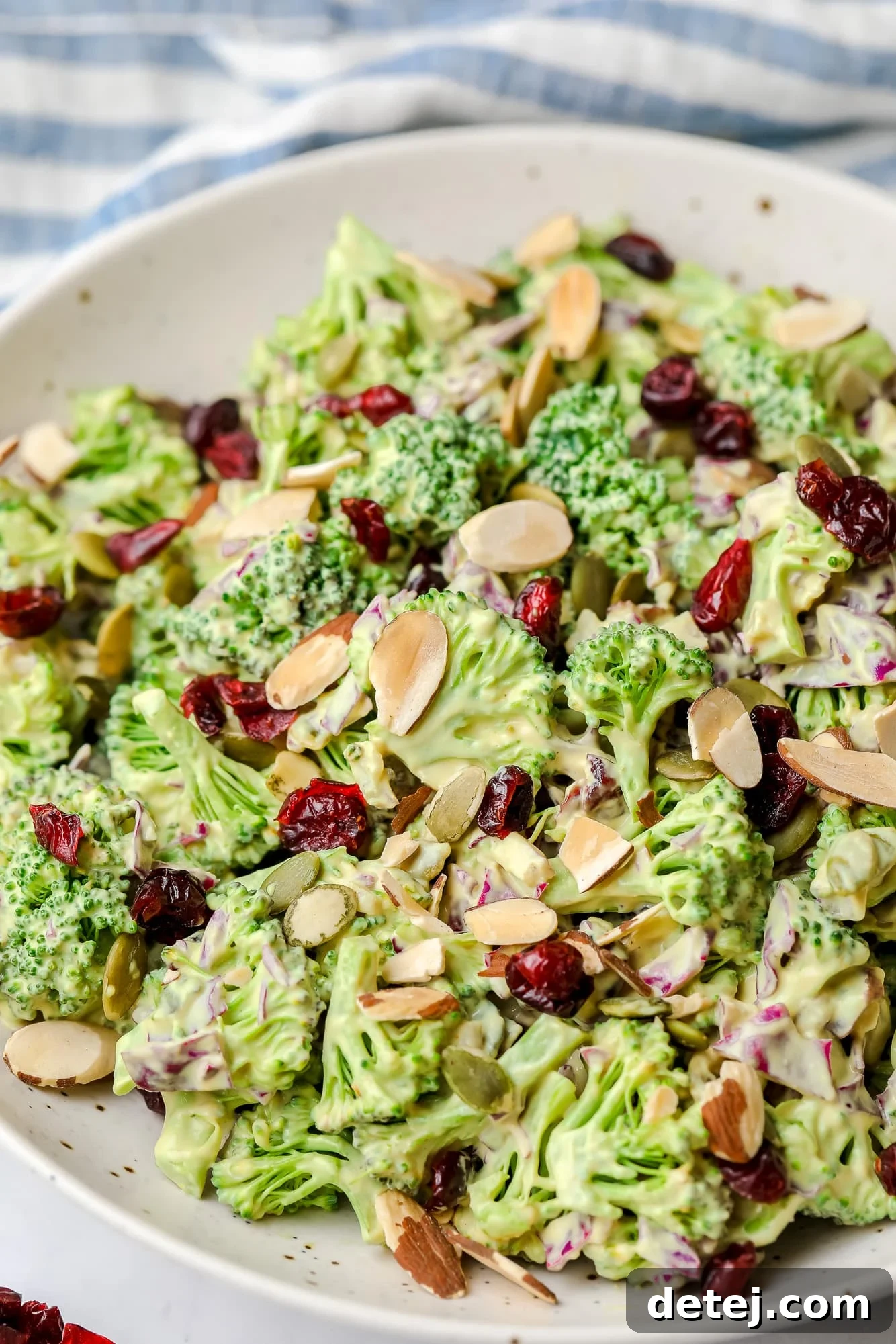 Close-up of vegan broccoli salad with creamy dressing and almonds in a large white serving bowl.