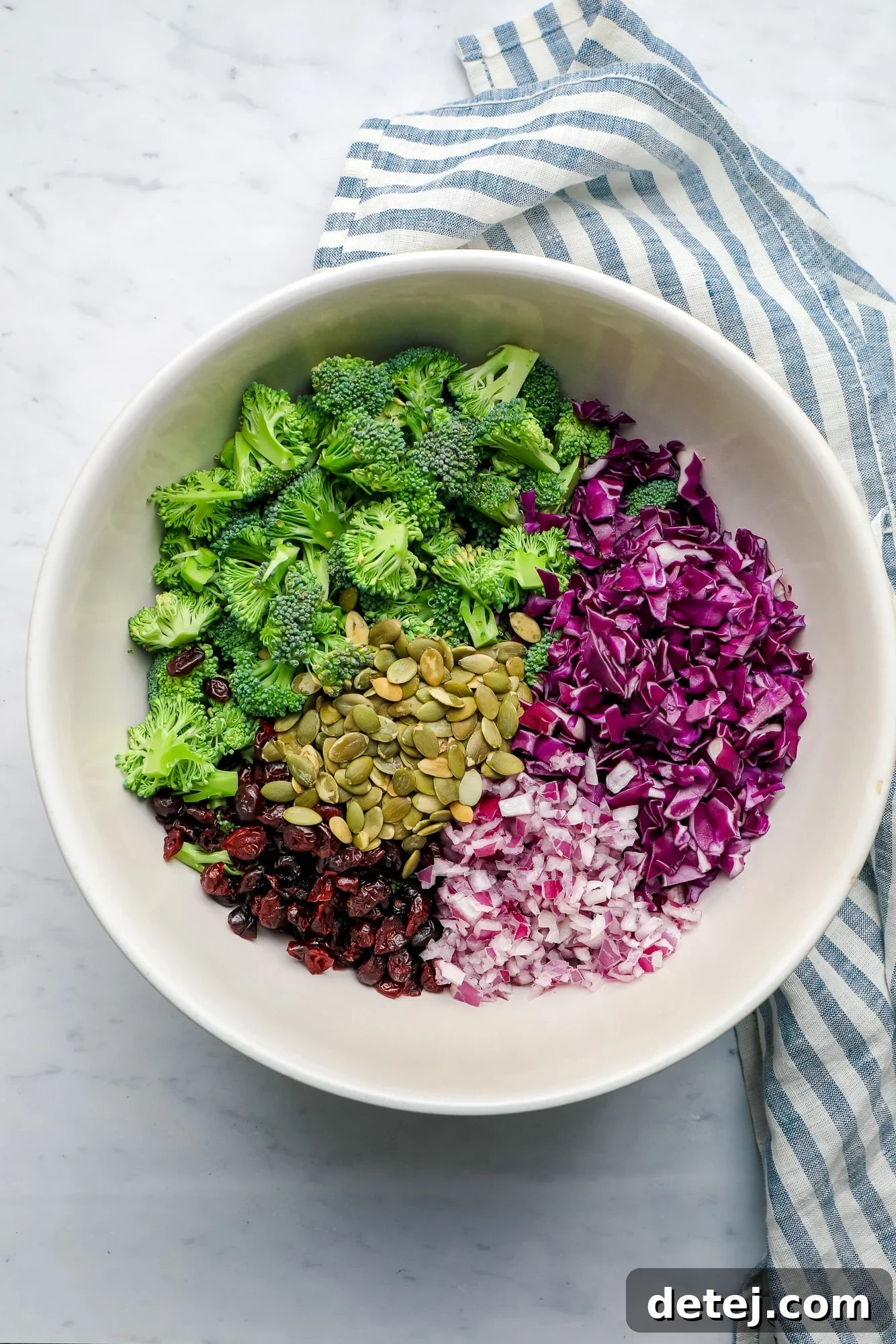 All the fresh ingredients for vegan broccoli salad arranged together in a large white bowl, before mixing.