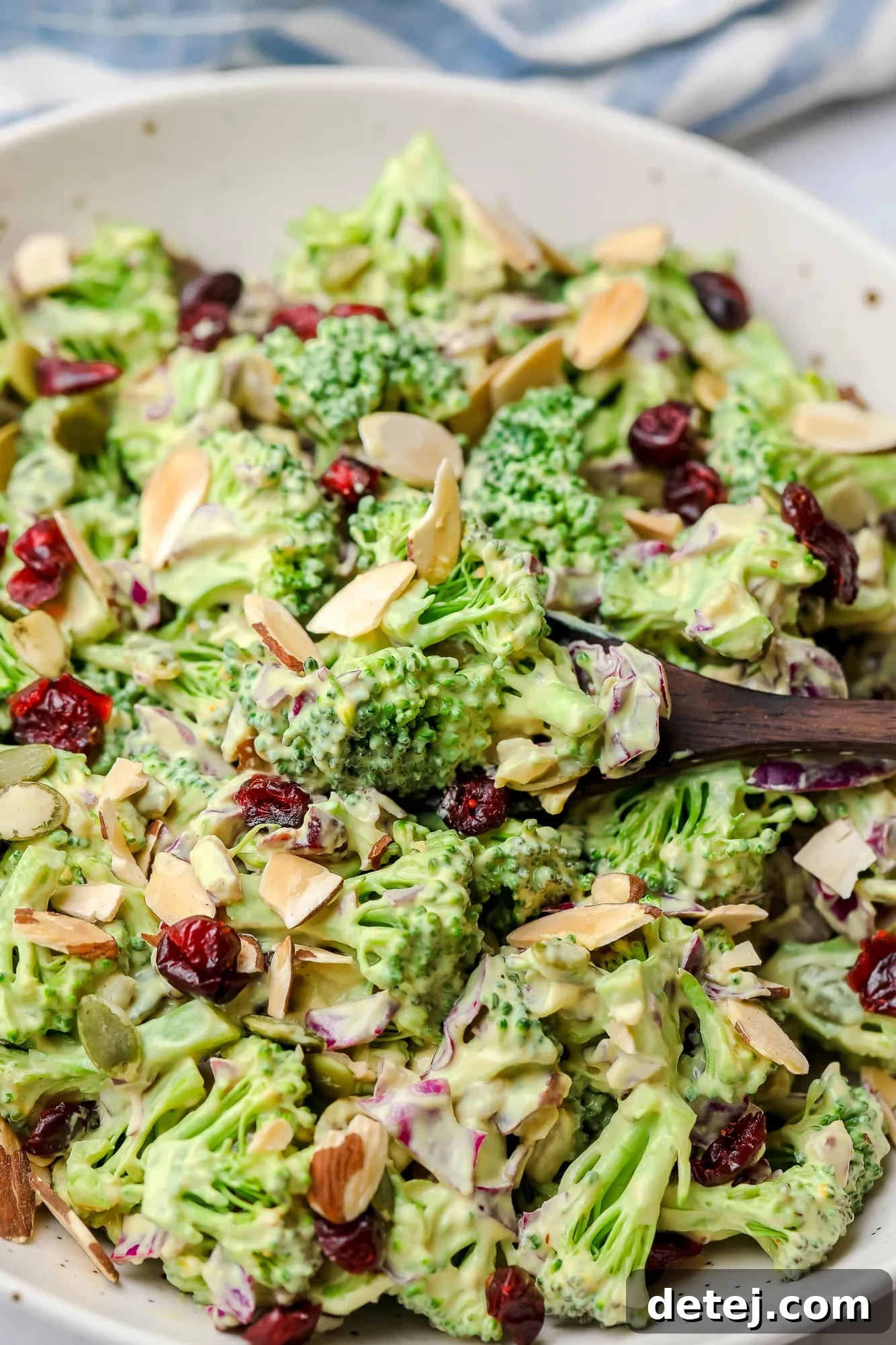 A wooden spoon scooping a portion of vegan broccoli salad from a large white bowl.