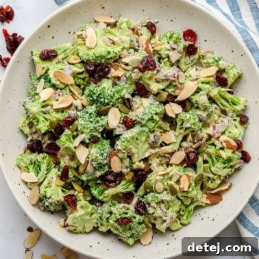 Close-up of vegan broccoli salad tossed in creamy dressing and topped with almonds in a large white bowl.