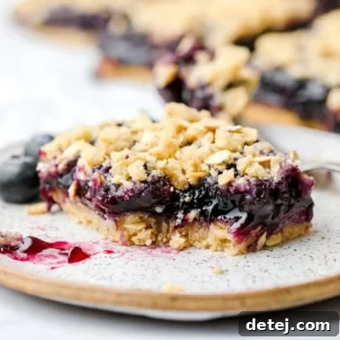 A square image of a vegan blueberry pie bar with oatmeal crumb topping, a bite taken out, resting on a speckled plate.