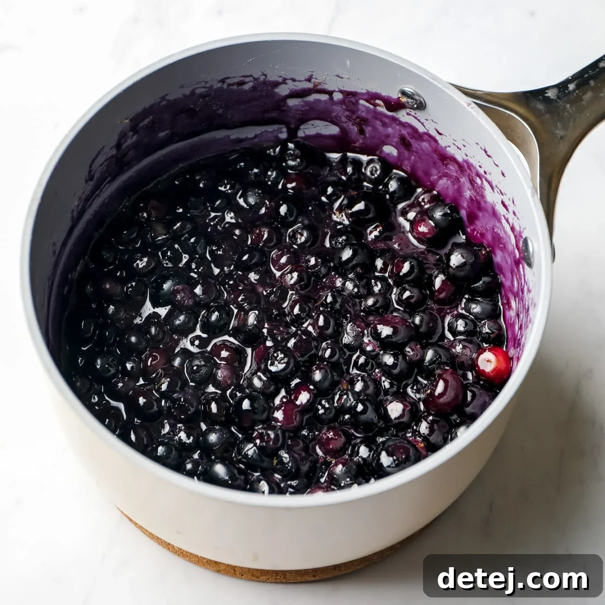 A small saucepan containing vibrant cooked blueberry mixture, visibly thickened, ready for layering.