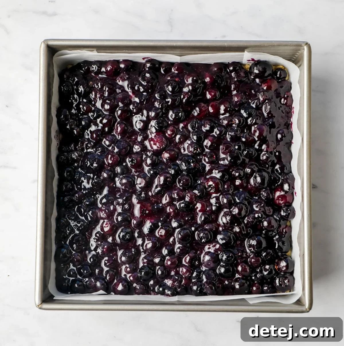 The cooked blueberry mixture spread evenly over the pre-baked crust in a square pan lined with parchment paper.
