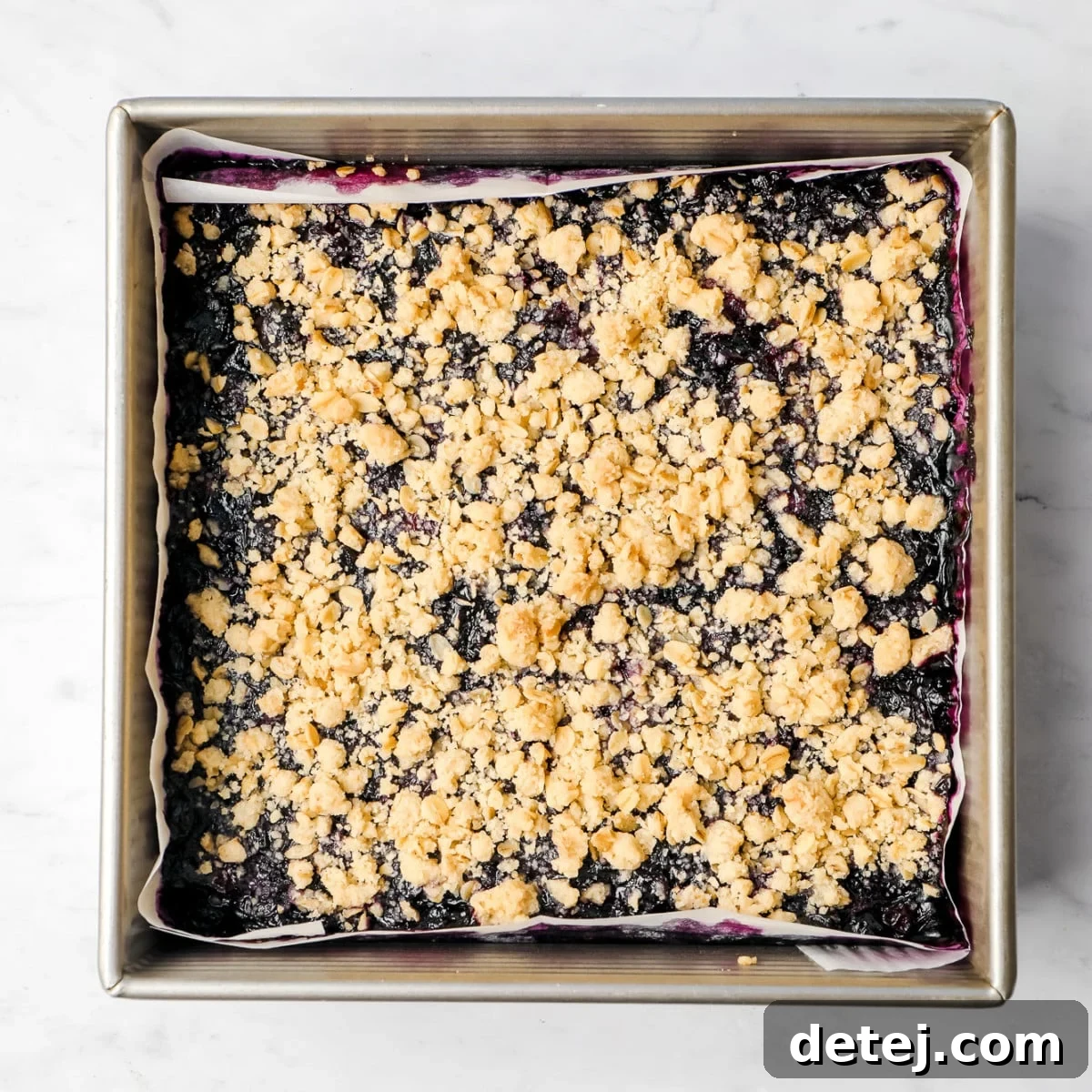 A square pan holding the perfectly baked blueberry pie bars, complete with a golden crumb topping over the bubbling blueberry mixture.