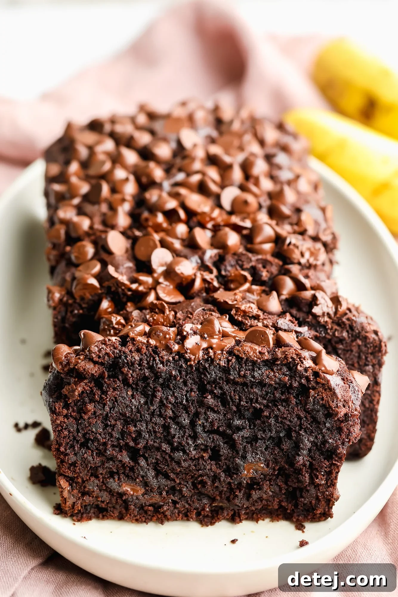 a sliced loaf of vegan chocolate banana bread on a white plate, showcasing its moist texture and abundant chocolate chips.