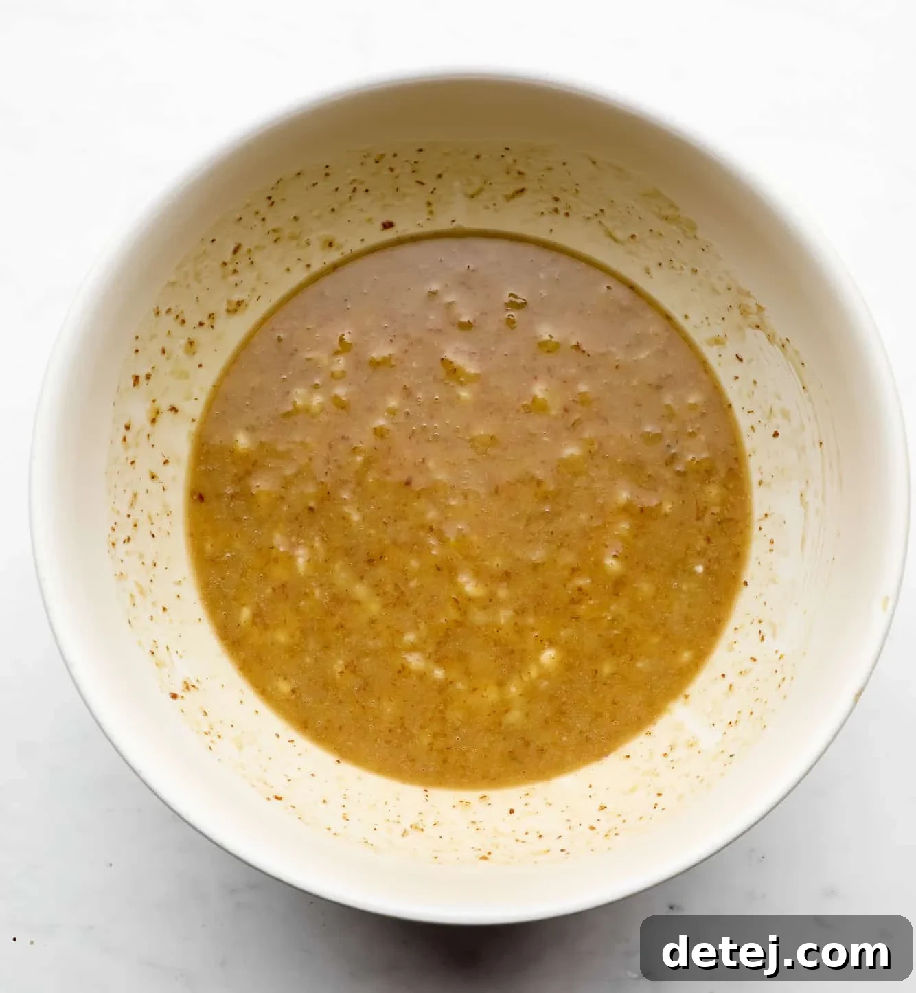 a light brown mashed banana mixture in a white bowl, showing the combined wet ingredients.