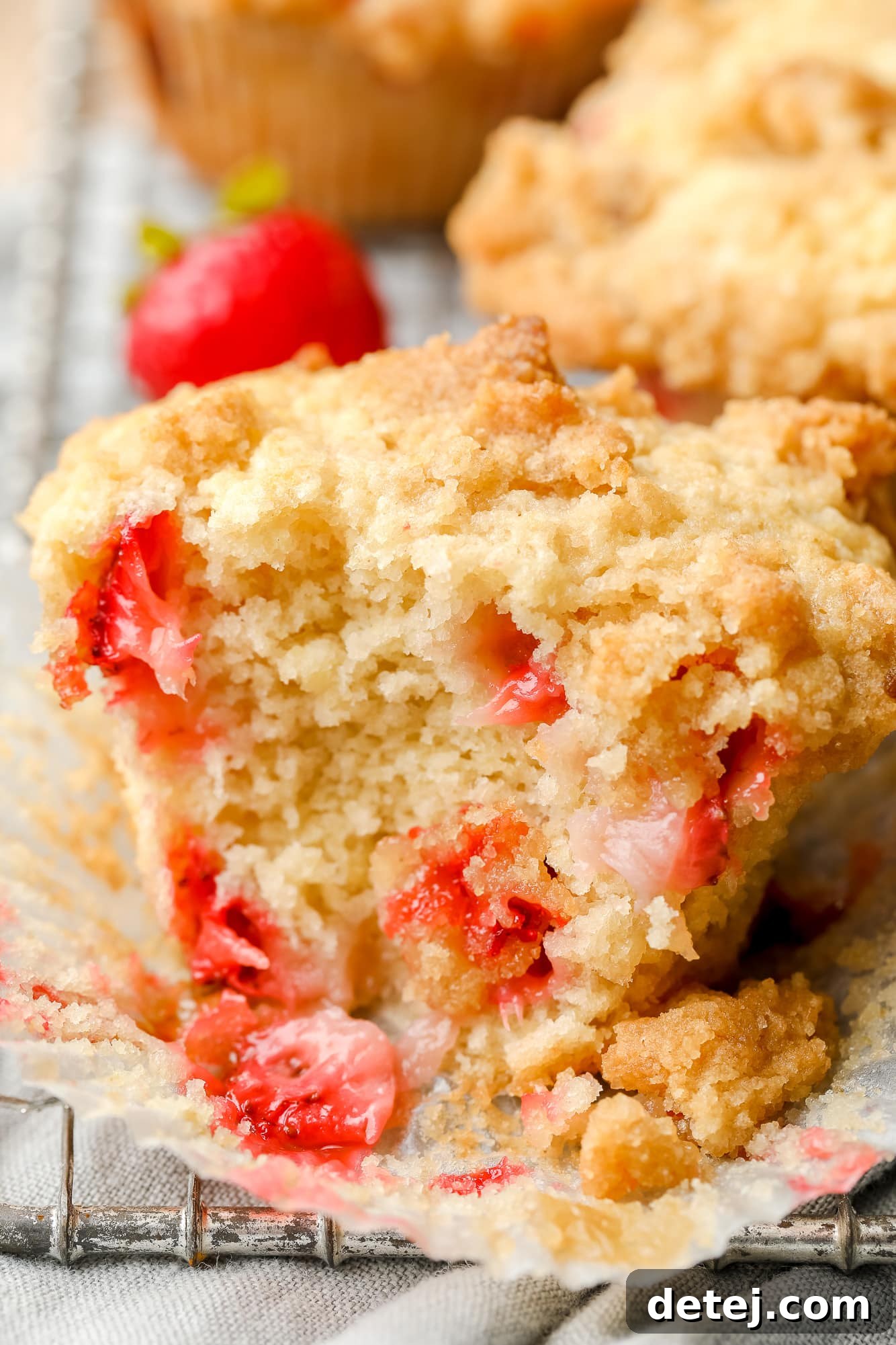 Luscious Vegan Strawberry Muffins 2 Close-up on a baked vegan strawberry muffin that's been split in half, revealing the fluffy interior and juicy strawberry pieces.