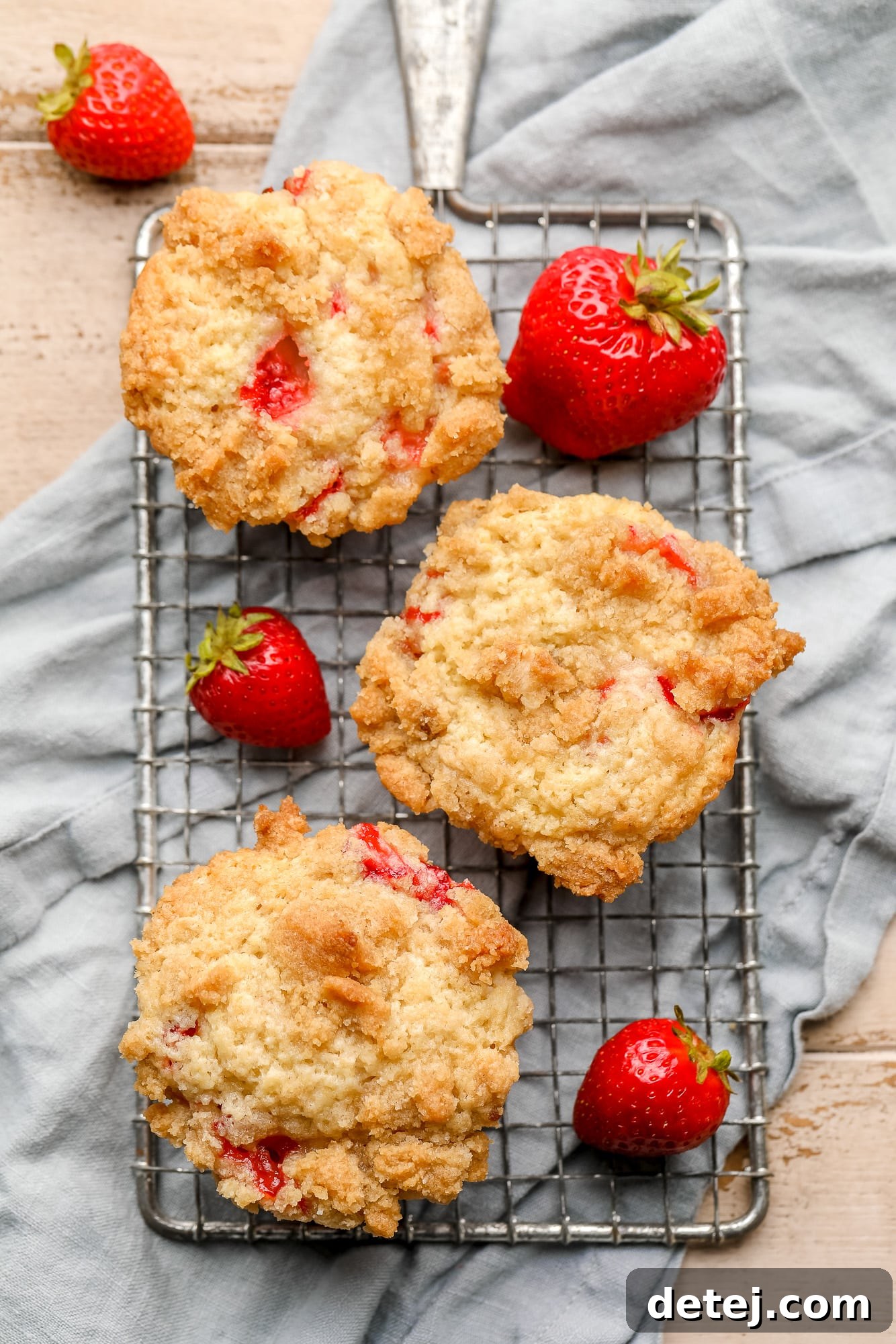 Luscious Vegan Strawberry Muffins 3 Three baked vegan strawberry muffins arranged on a small wire rack, surrounded by fresh strawberries.