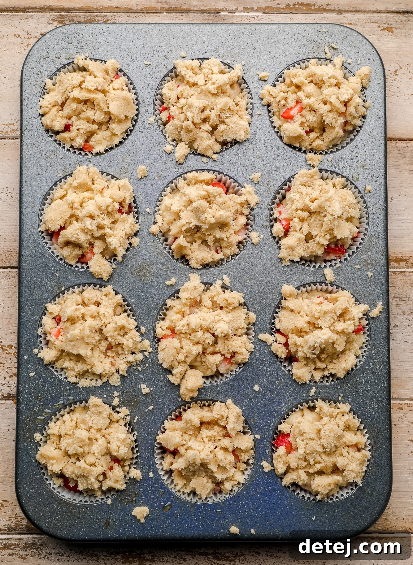 Luscious Vegan Strawberry Muffins 5 A muffin tin filled with unbaked vegan strawberry muffin batter, generously topped with a sweet crumble.