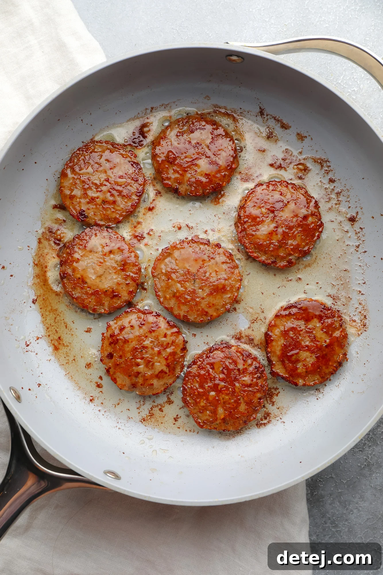 Vegan breakfast sausage rounds sizzling beautifully in a large grey skillet on the stovetop.
