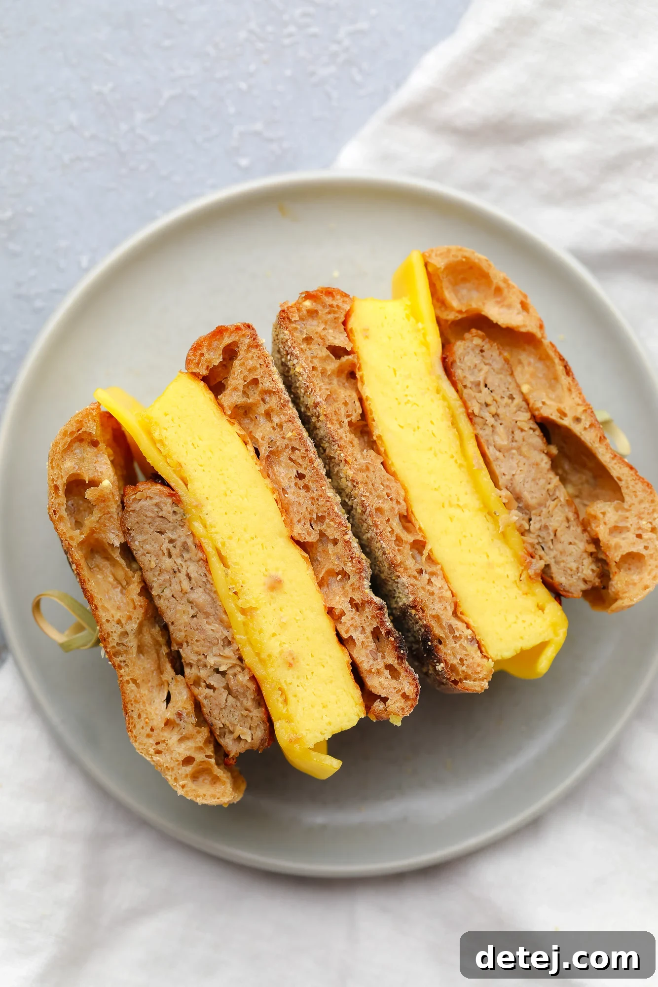A vegan breakfast sandwich, perfectly cut in half to reveal its layers, resting on a stylish grey plate.