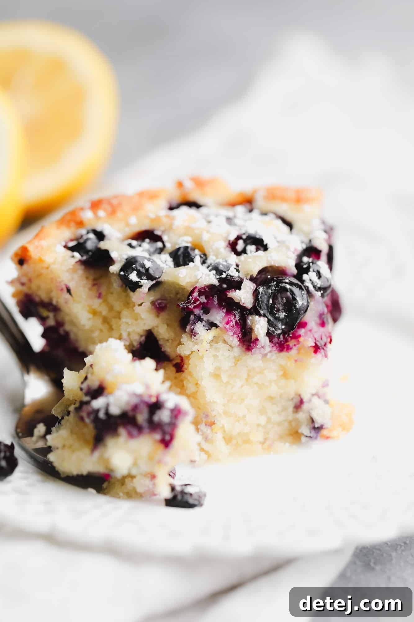 close up on a slice of vegan blueberry cake with a bite missing on a white plate.
